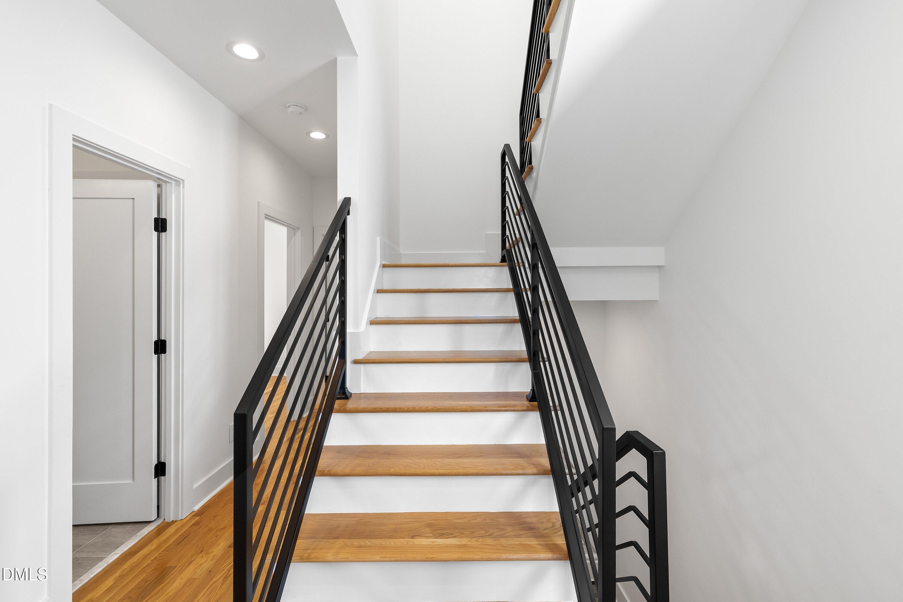 Modern staircase with wood treads, white risers, and black metal railings.