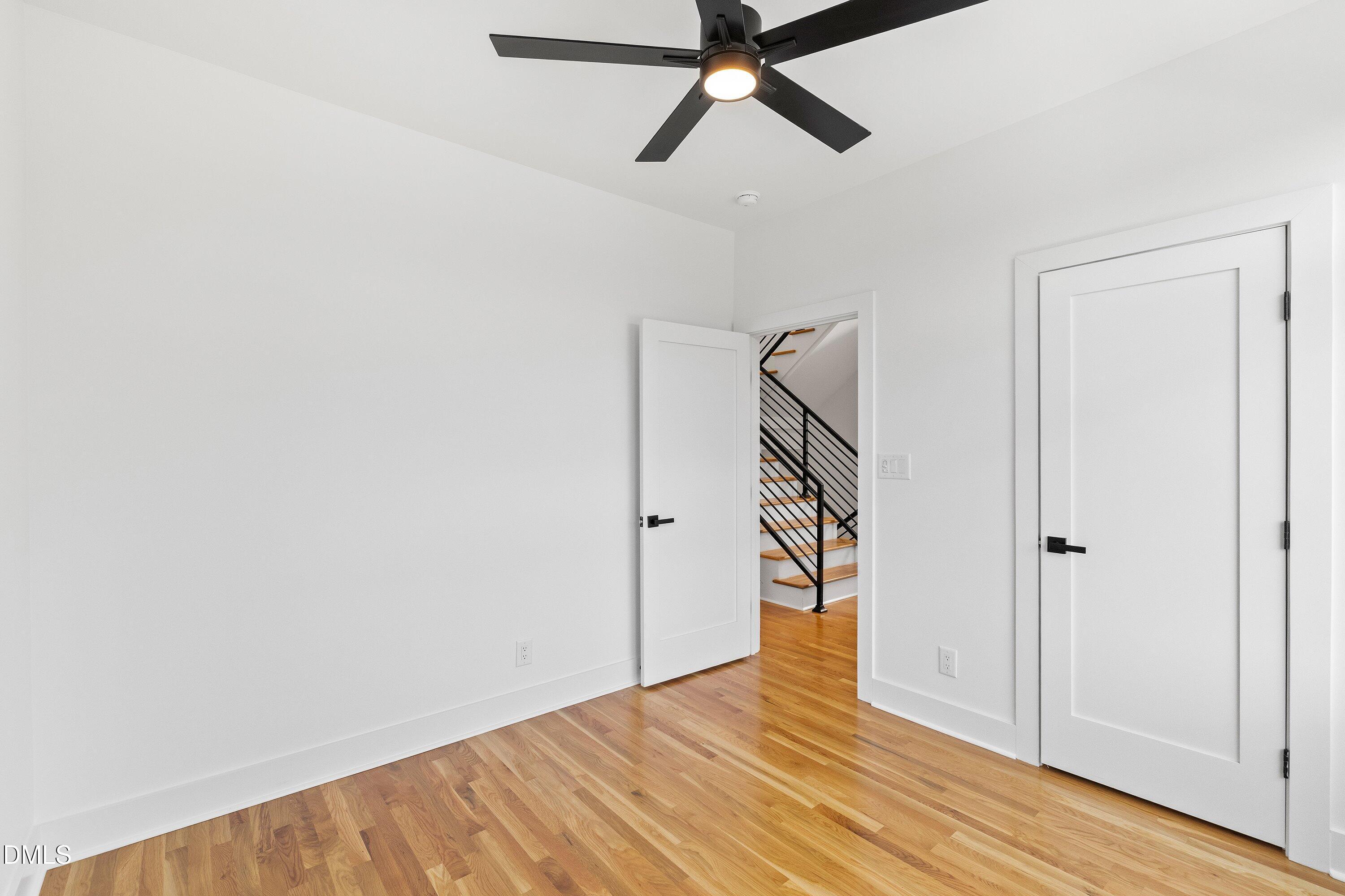 Empty room with hardwood floors, a black ceiling fan, and a doorway overlooking a staircase.