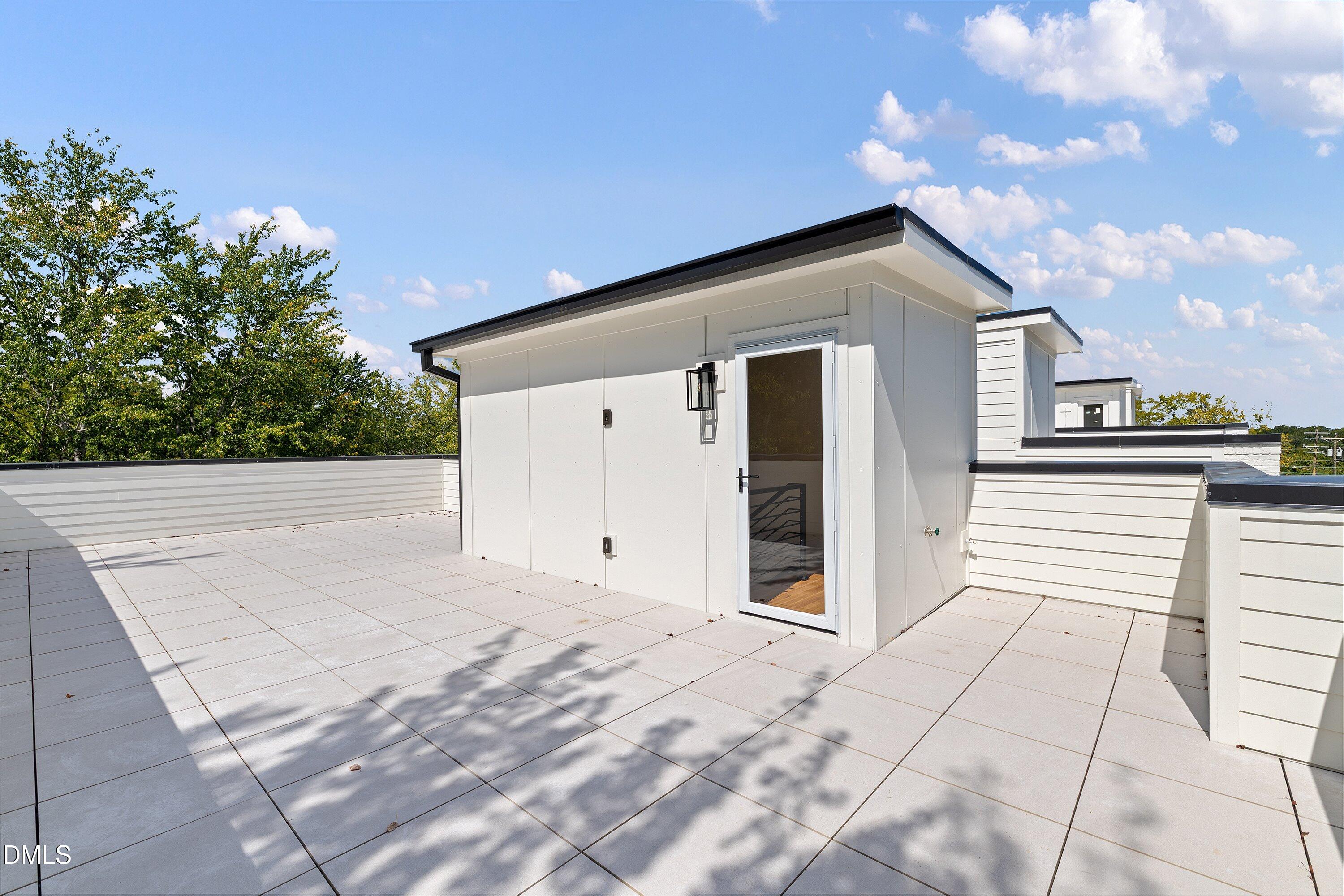 Rooftop terrace with light tiled flooring, white parapet walls, and a modern rooftop structure.