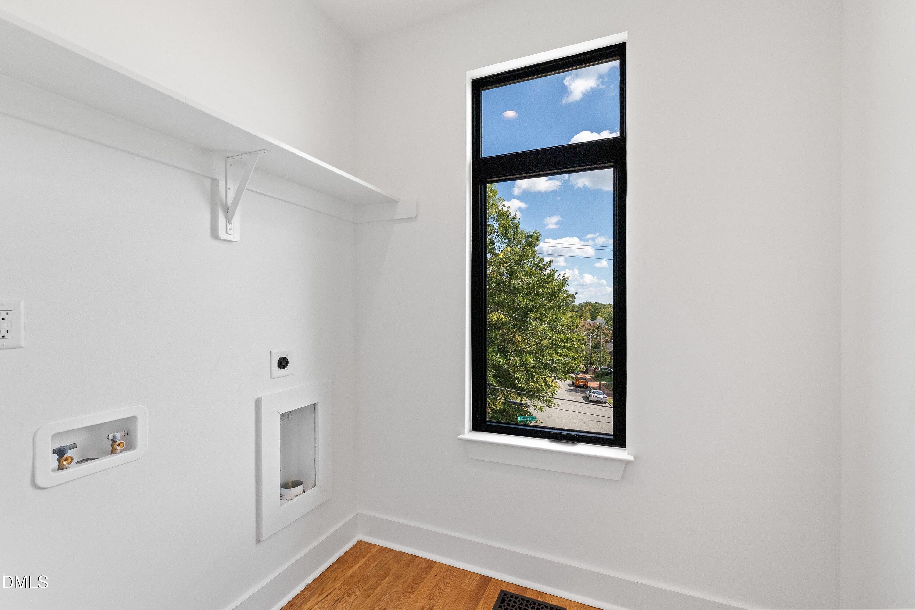 Laundry room with washer hookups, a wall shelf, hardwood floor, and a tall window overlooking trees.