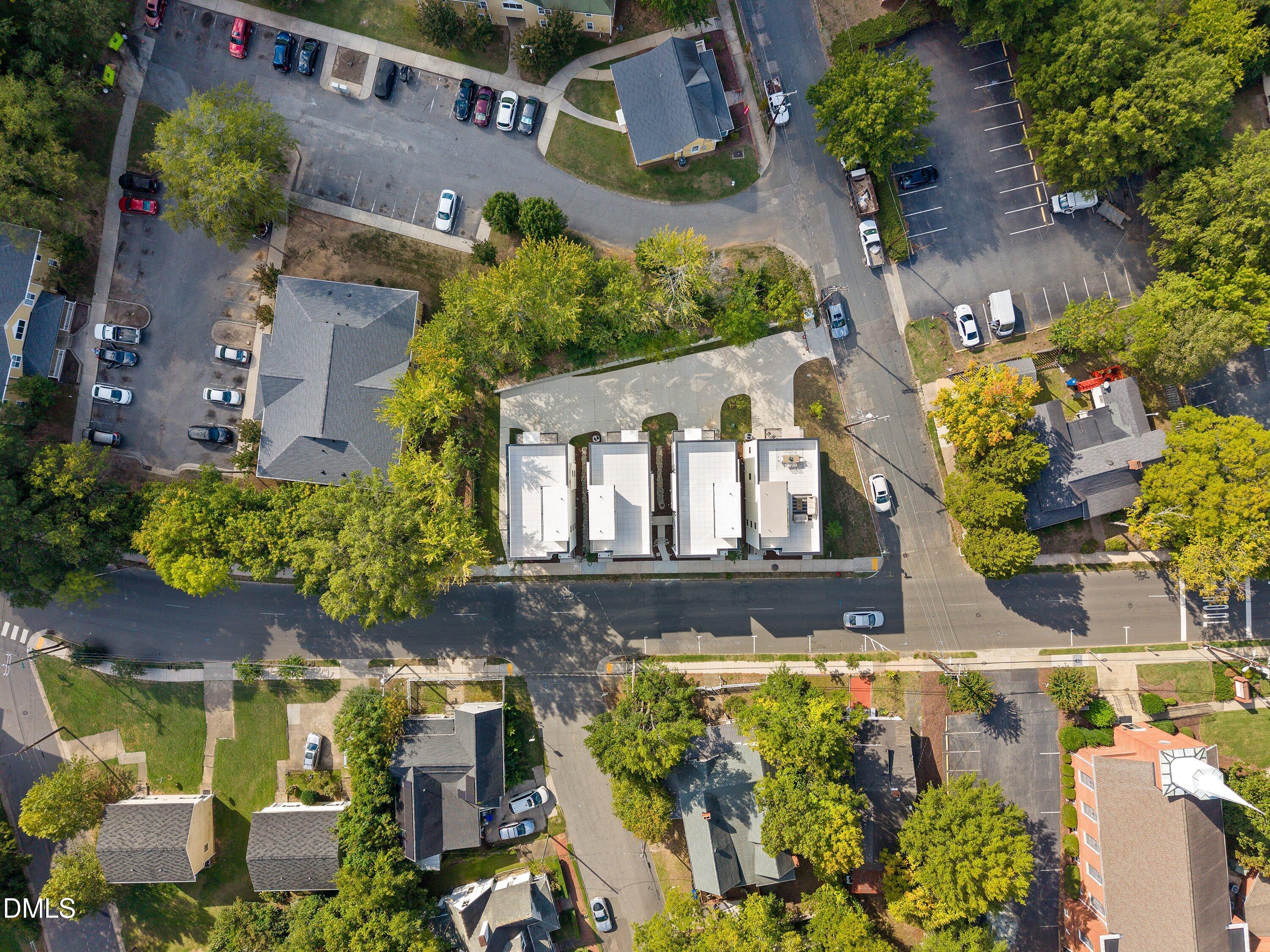 Aerial view of four flat-roofed buildings in a row, surrounded by trees and urban streets.