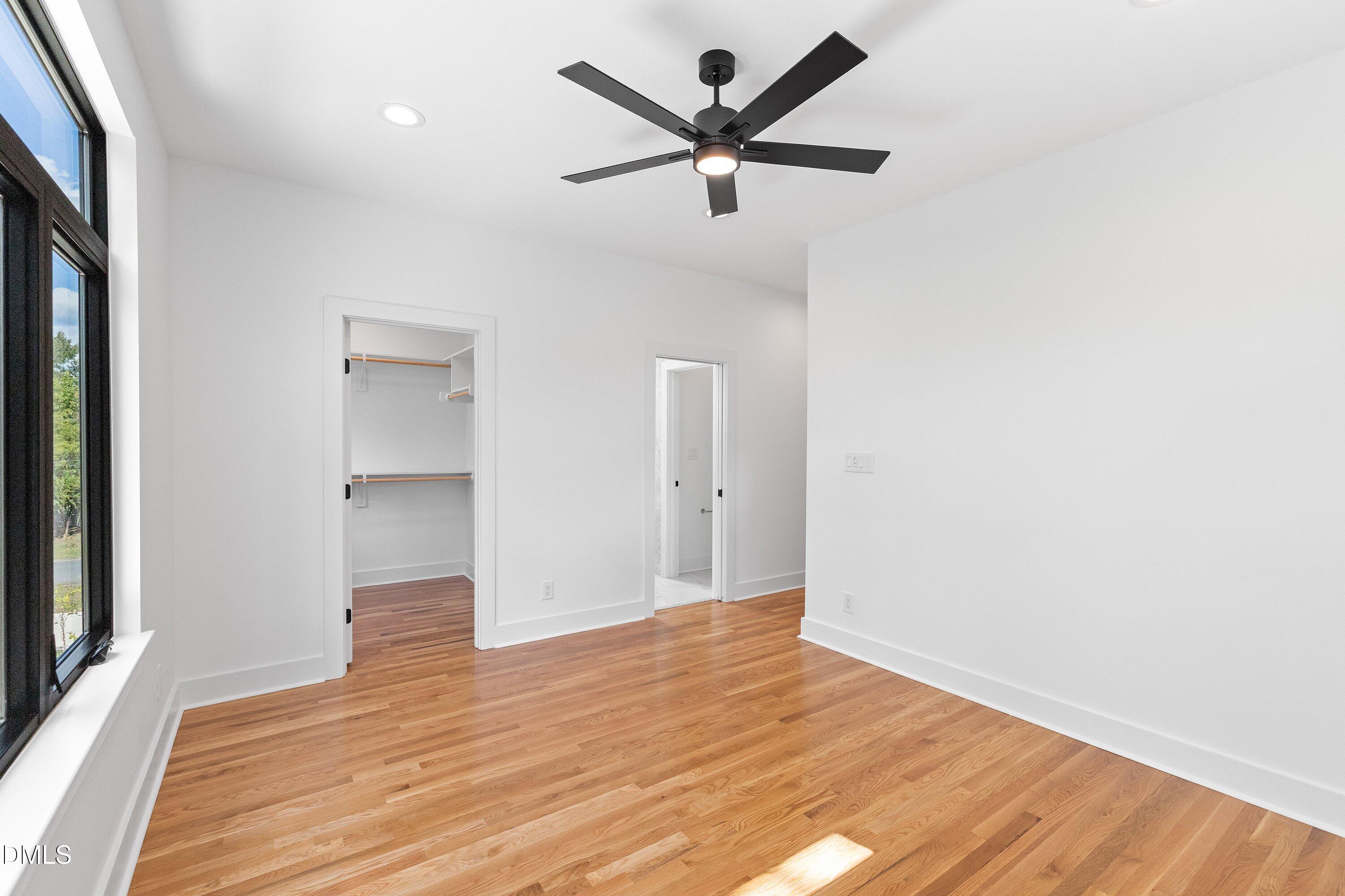 Vacant bedroom with hardwood floors, a large black-framed window, and an open closet.