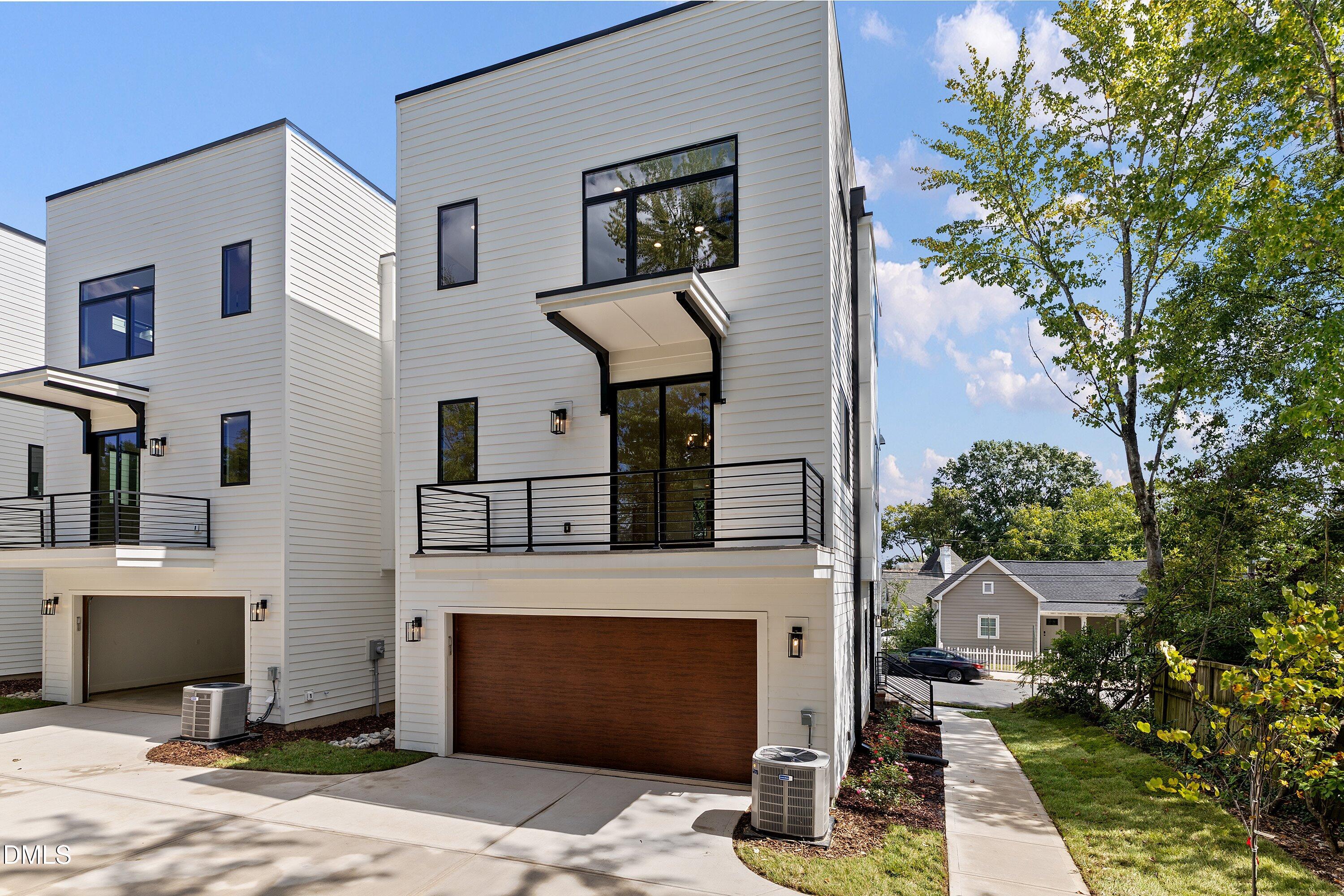 Contemporary white townhome exterior with black railings, balconies, and wood-toned garage doors.