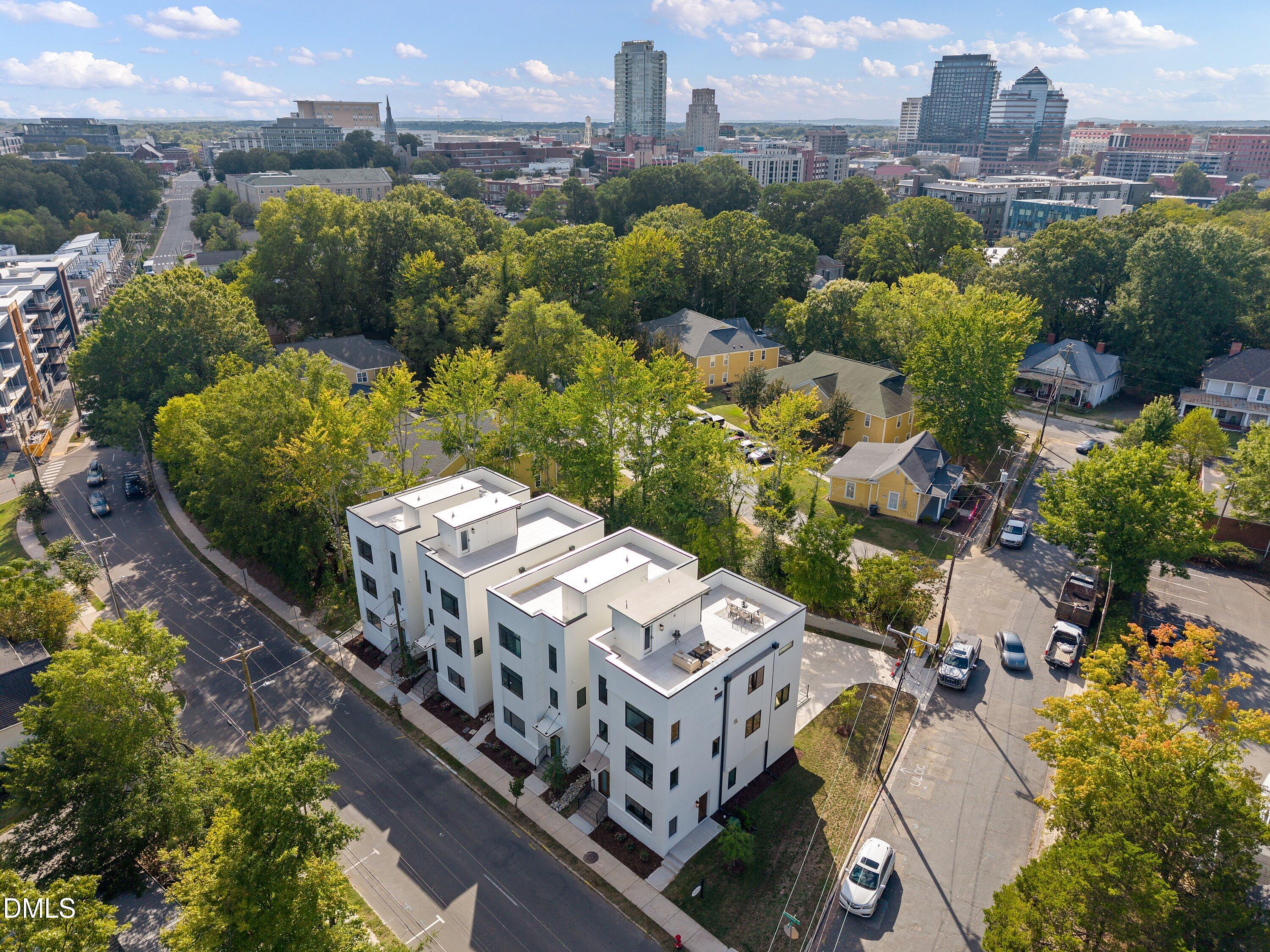 Modern white townhomes with rooftop terraces amid leafy streets, with the Durham skyline beyond.