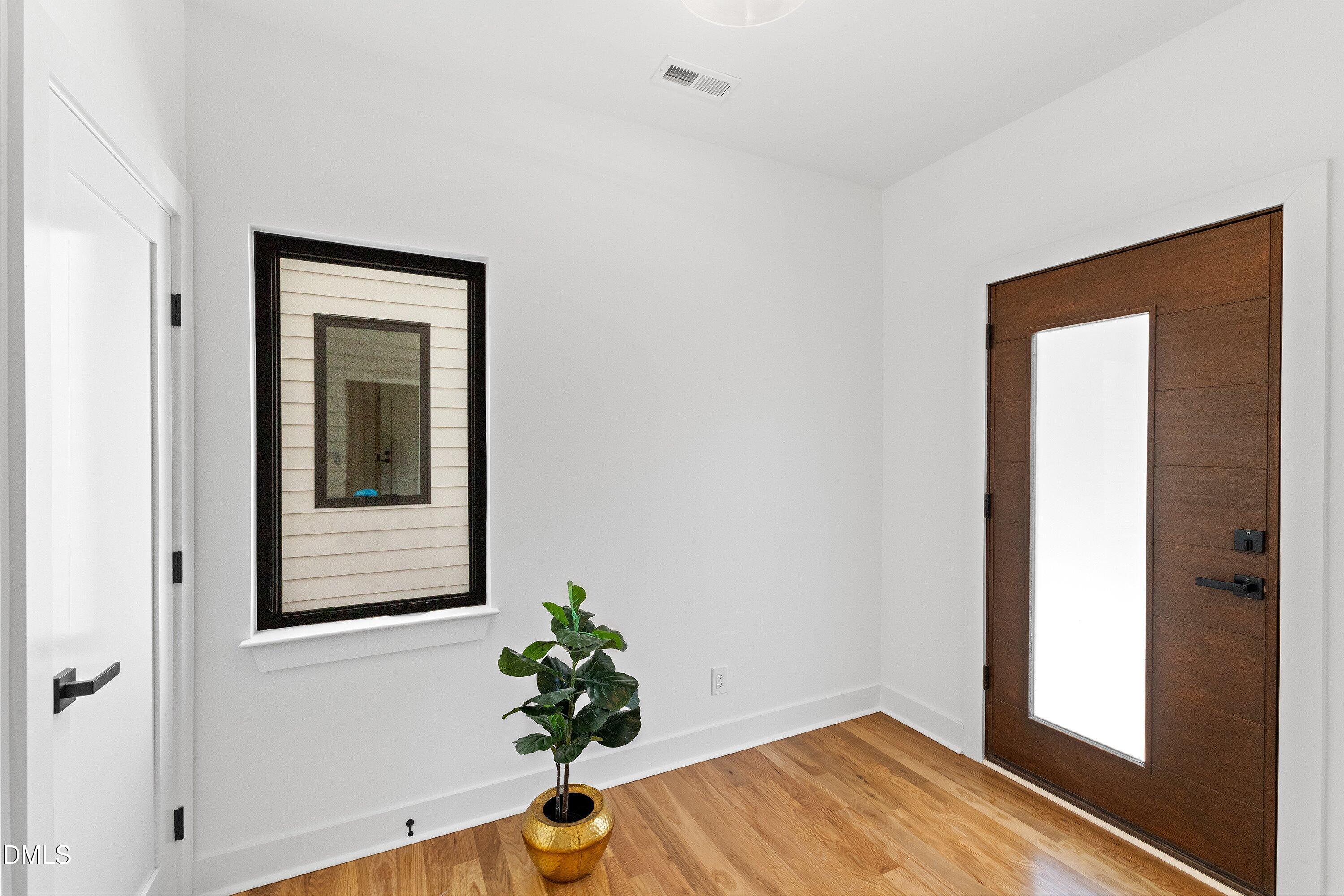 Entry foyer with a wood front door, warm wood floors, and a potted plant.
