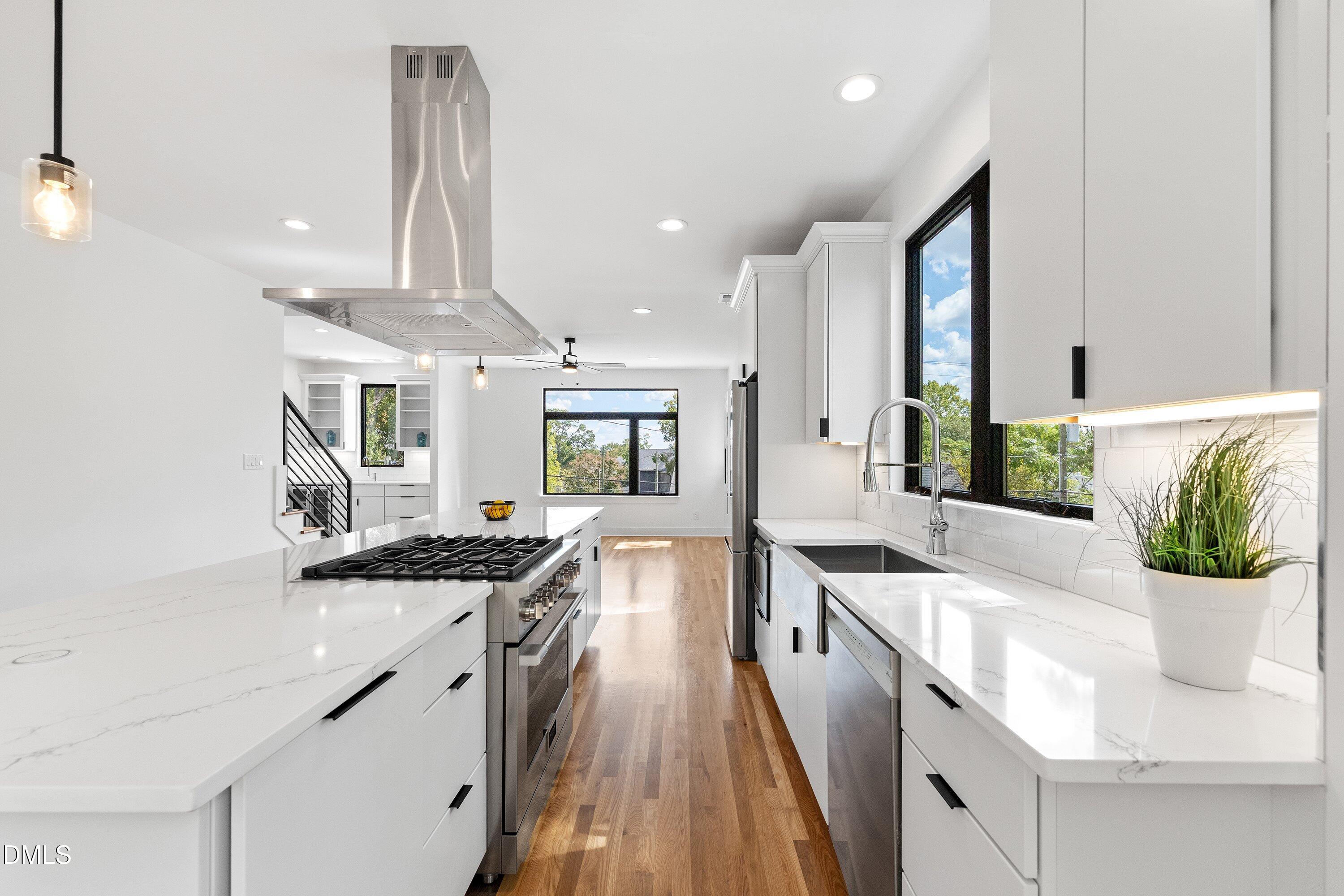 Modern white kitchen with a gas cooktop island, quartz counters, hardwood floors, and tall black-framed windows.