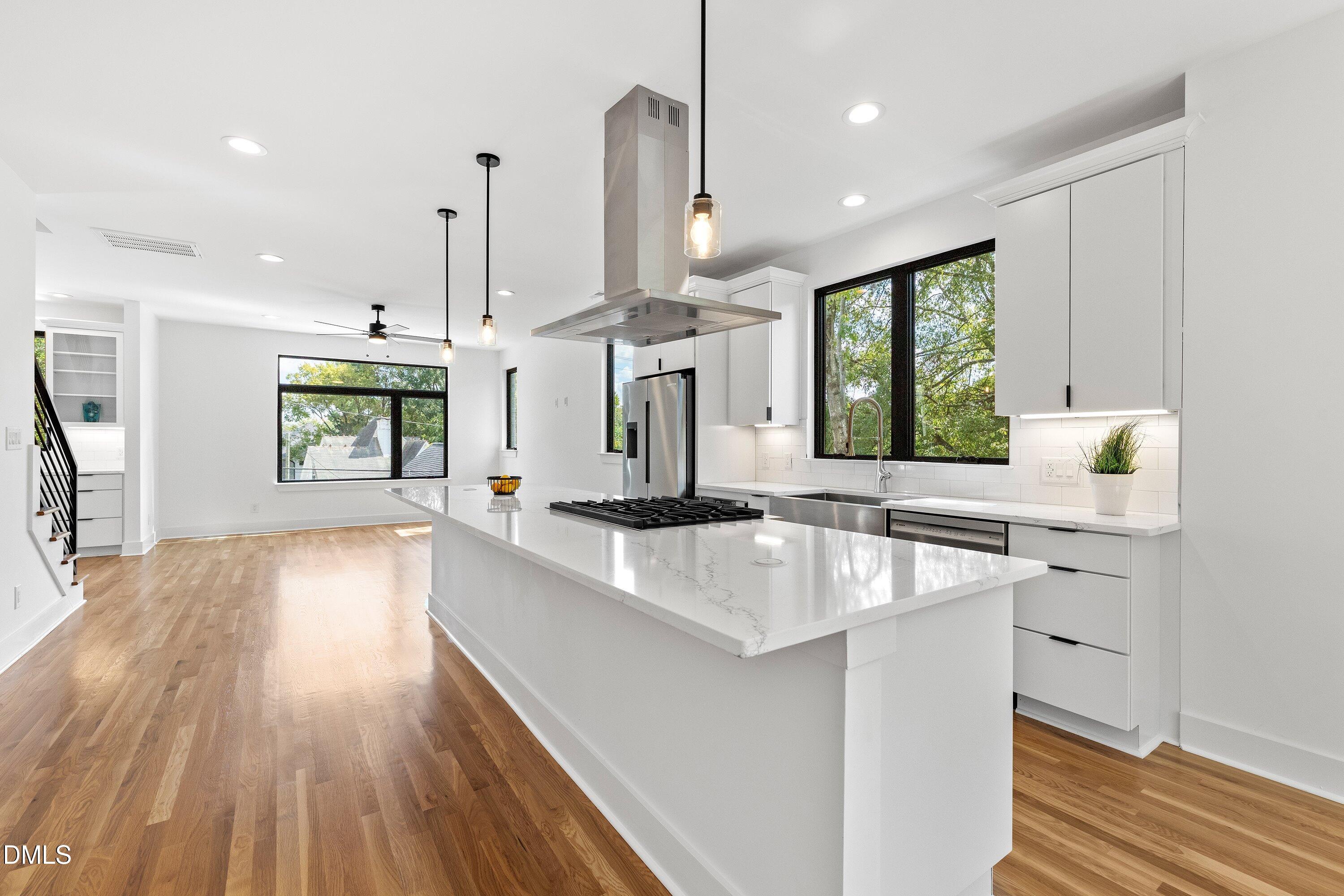 Bright open kitchen with a large white island, gas cooktop, stainless appliances, and warm wood floors.