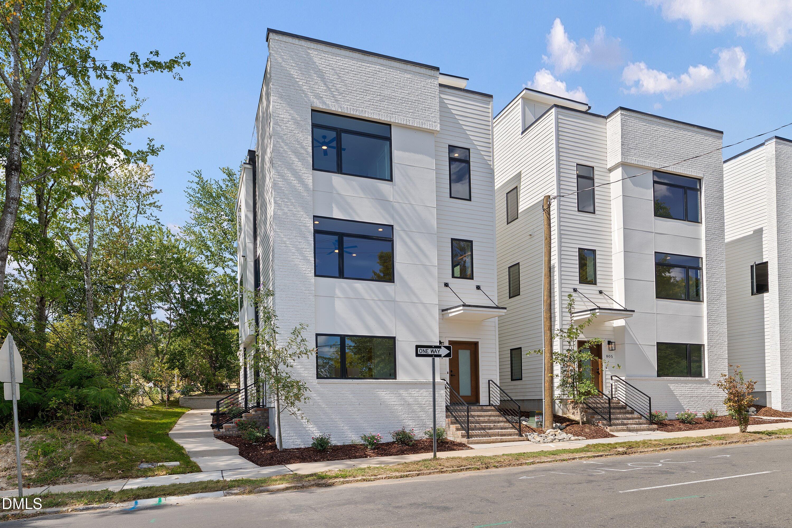Modern white townhomes with black-framed windows and landscaped front entrances along a sidewalk.