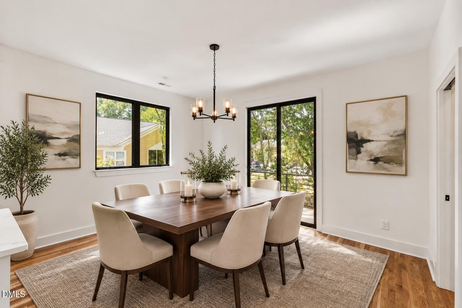 Dining room with a dark wood table, upholstered chairs, black chandelier, and large windows.