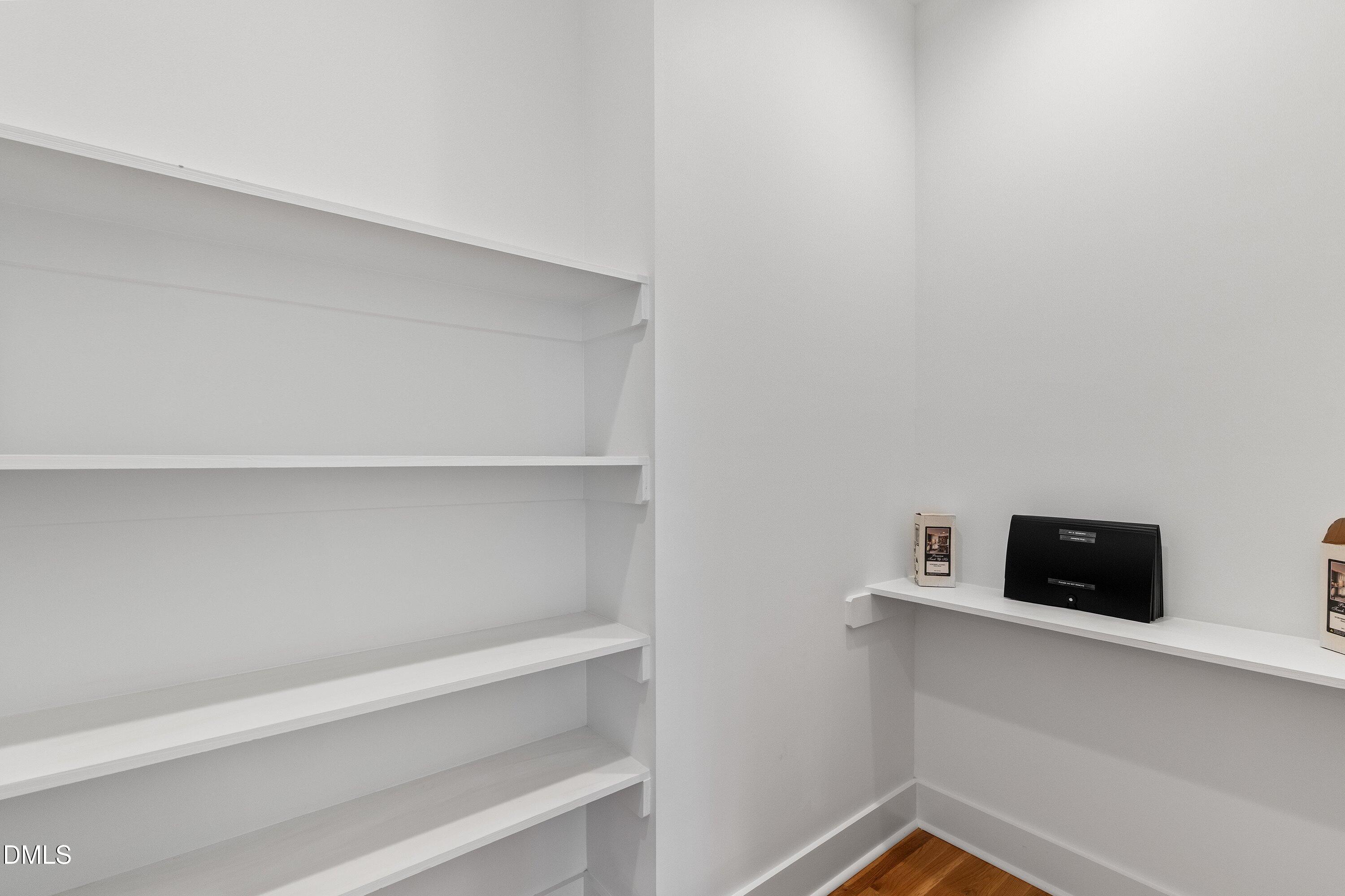 Storage room with white built-in shelves, a black organizer, and a glimpse of hardwood flooring.
