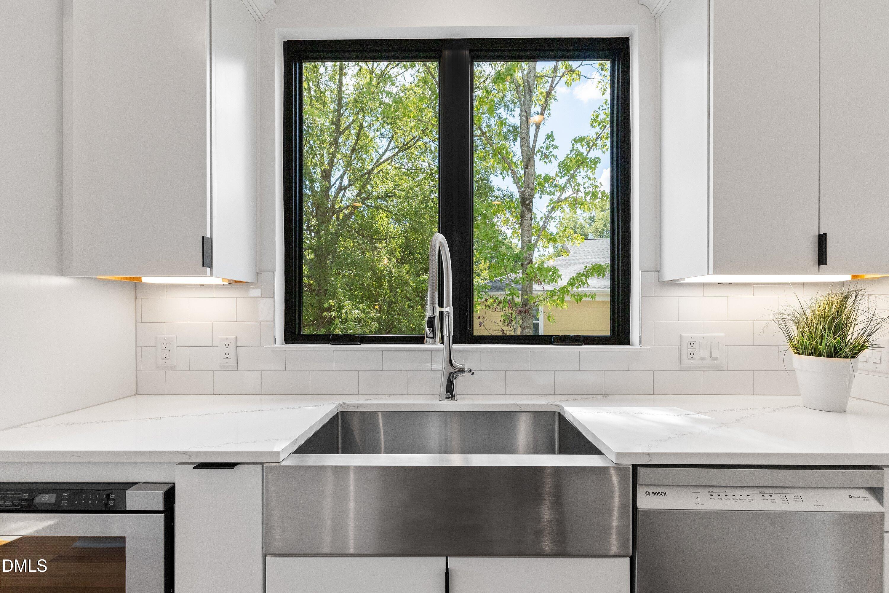 Modern kitchen with a large stainless steel sink beneath a window and white cabinetry.
