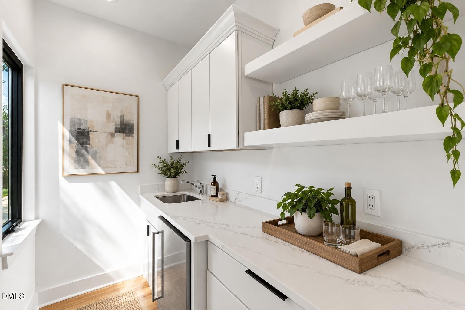 Bright kitchen with white cabinets, open shelves, veined countertops, and sunlight from a tall window.