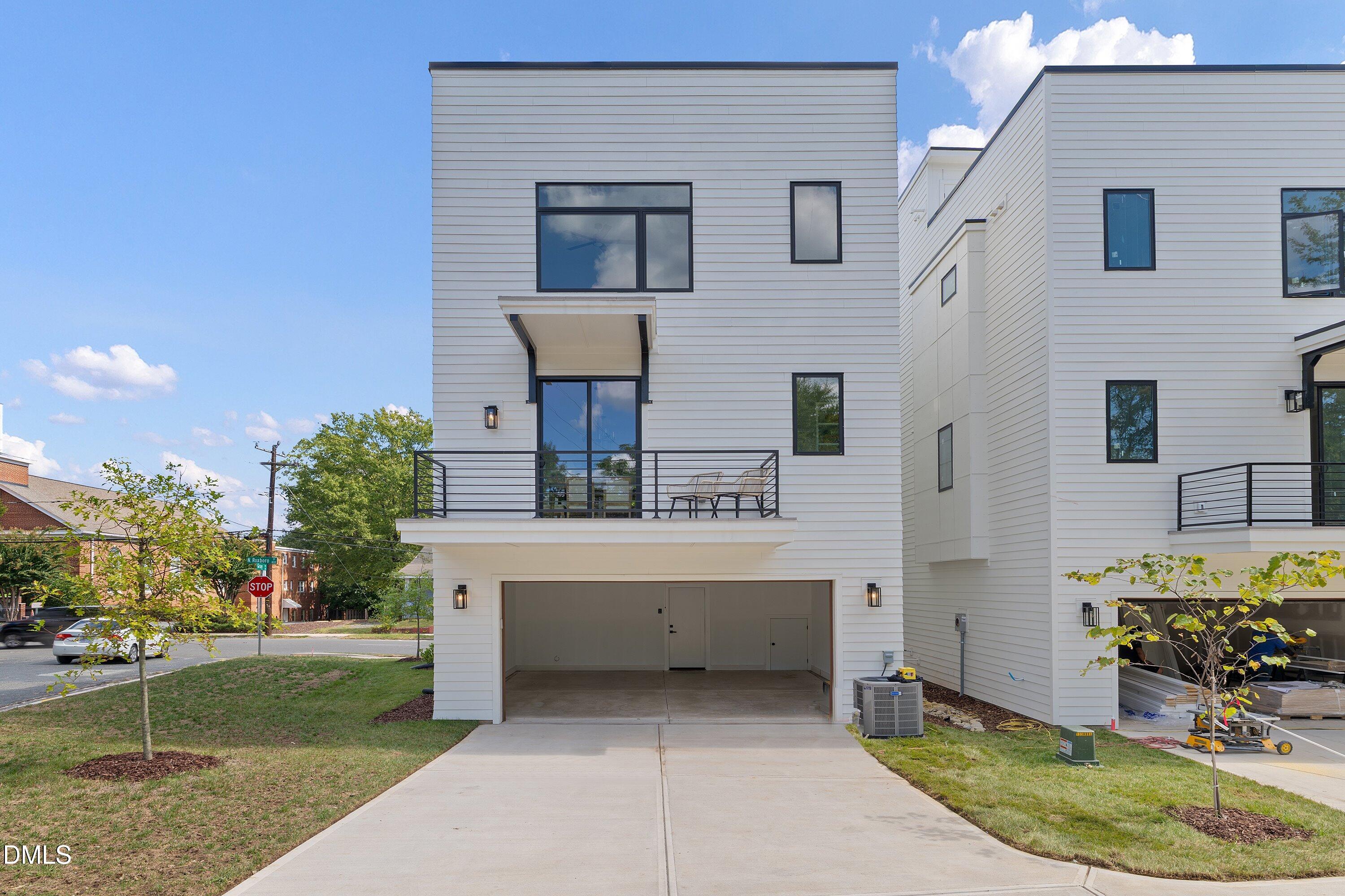 Modern white townhouse with a black-railed balcony above an open garage and neighboring home.