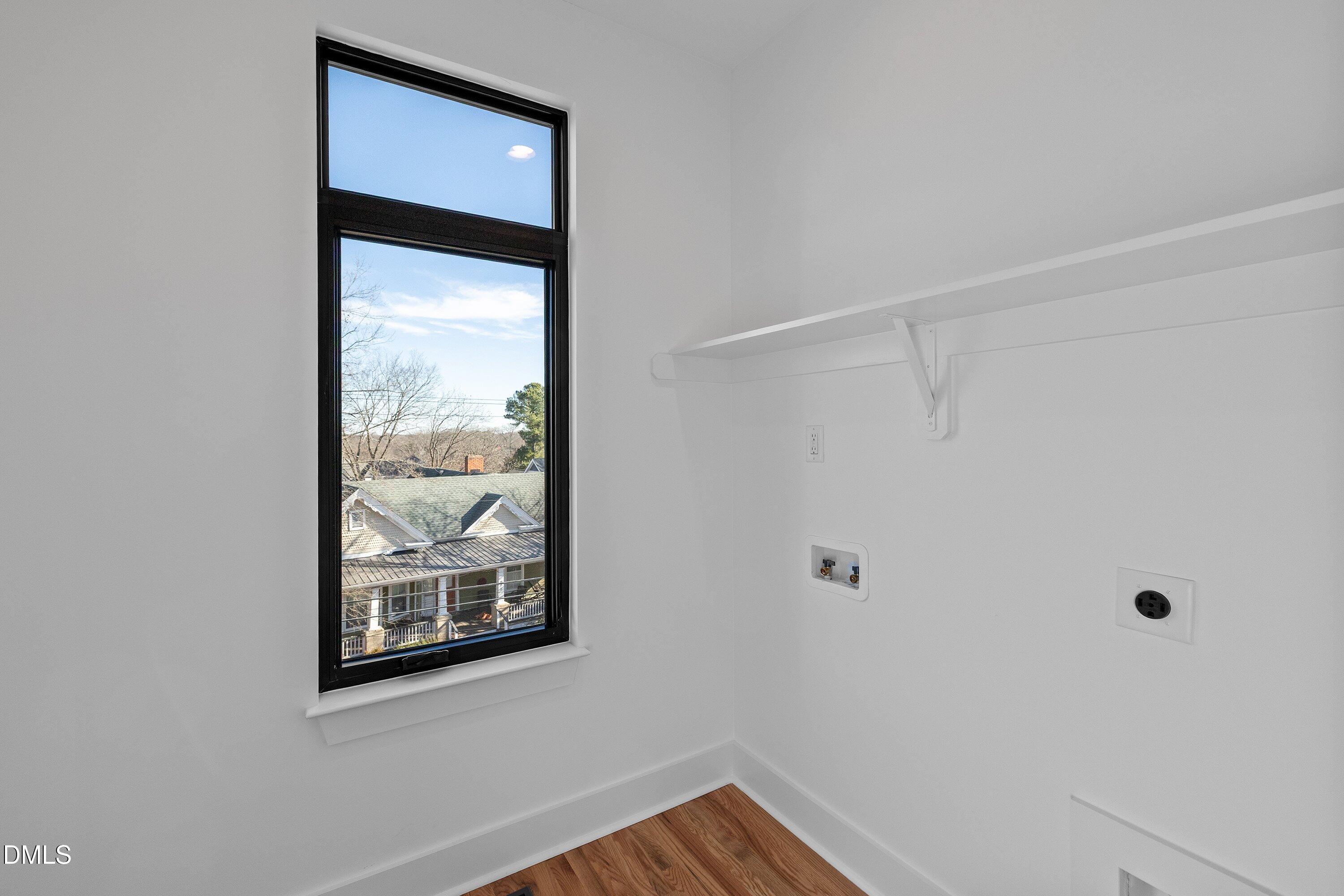 Vacant laundry room with a tall window, white shelf, laundry hookups, and wood flooring.