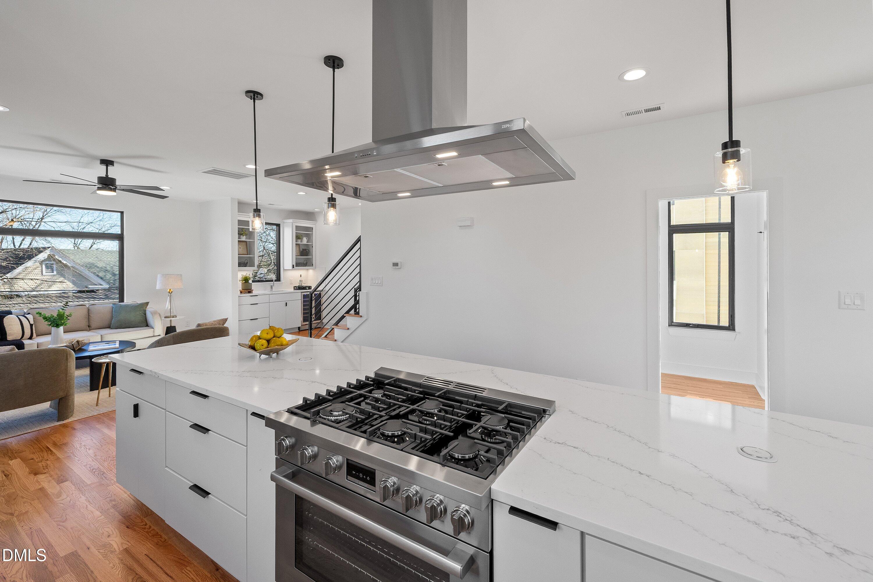 Open kitchen with a large quartz island, stainless steel gas range, and view into the living area.