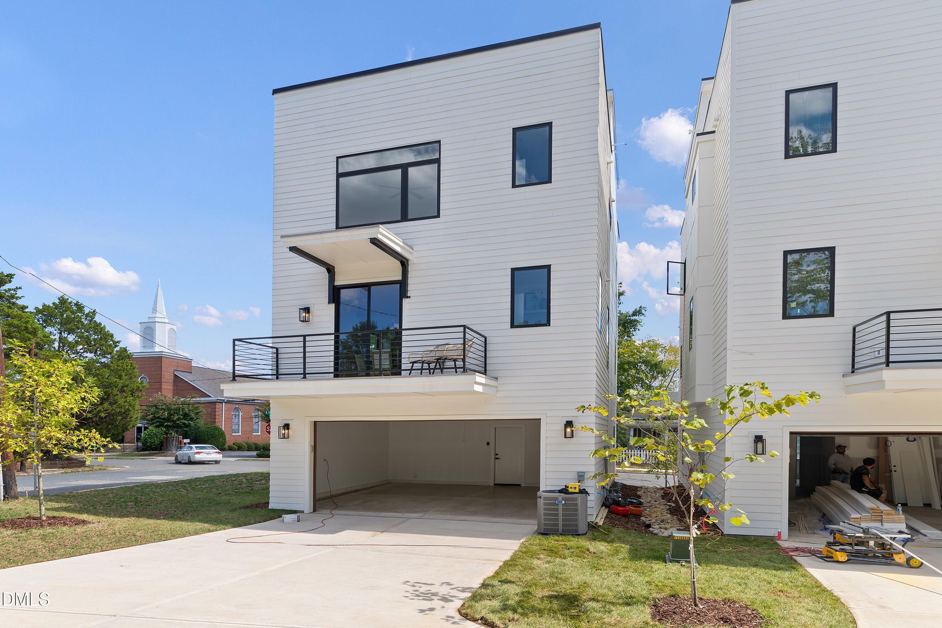 Modern white townhouse with black-trimmed windows, a balcony, and an open garage.