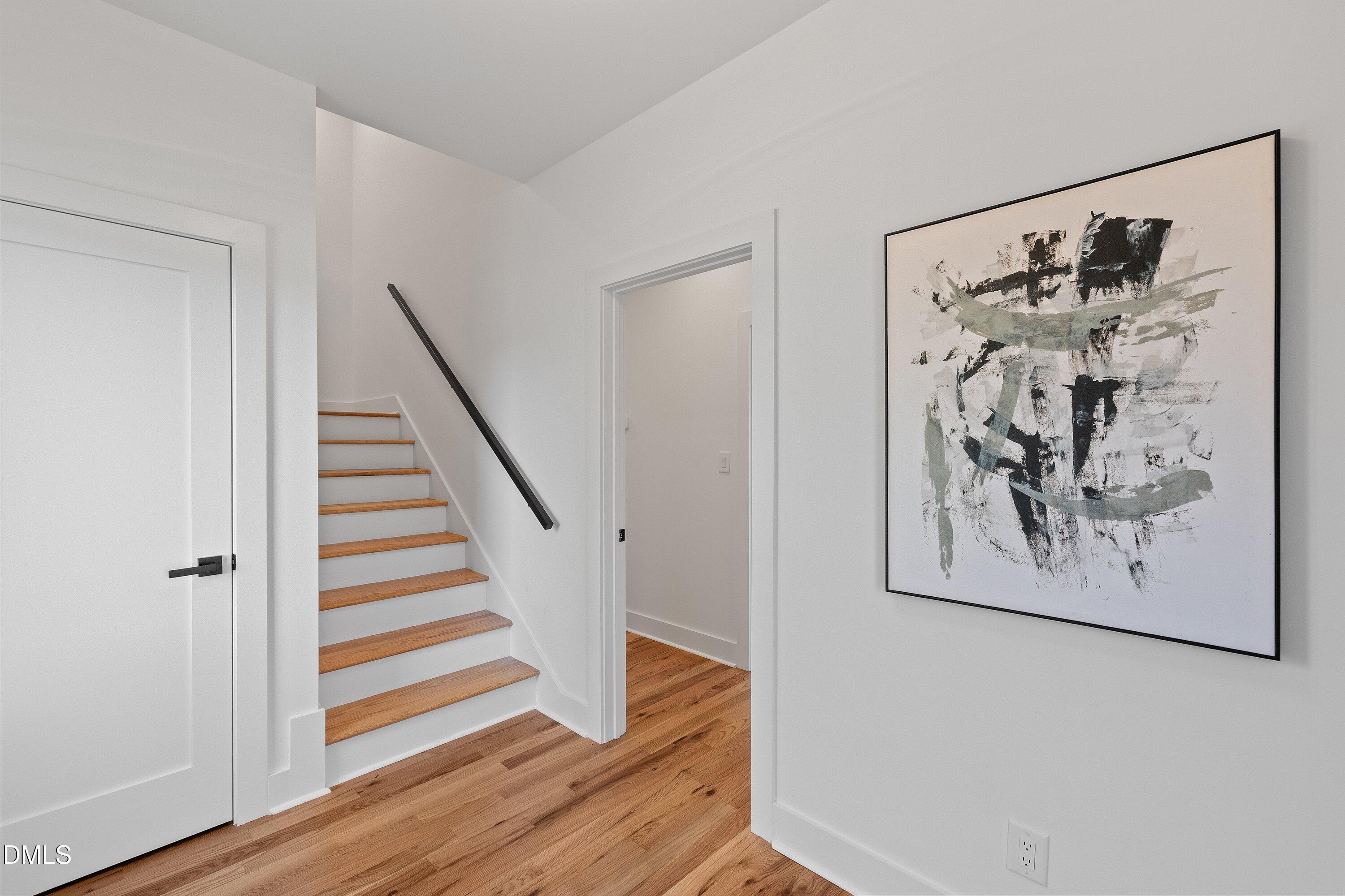 Bright hallway with wood-tread stairs, a black handrail, and a large abstract painting.