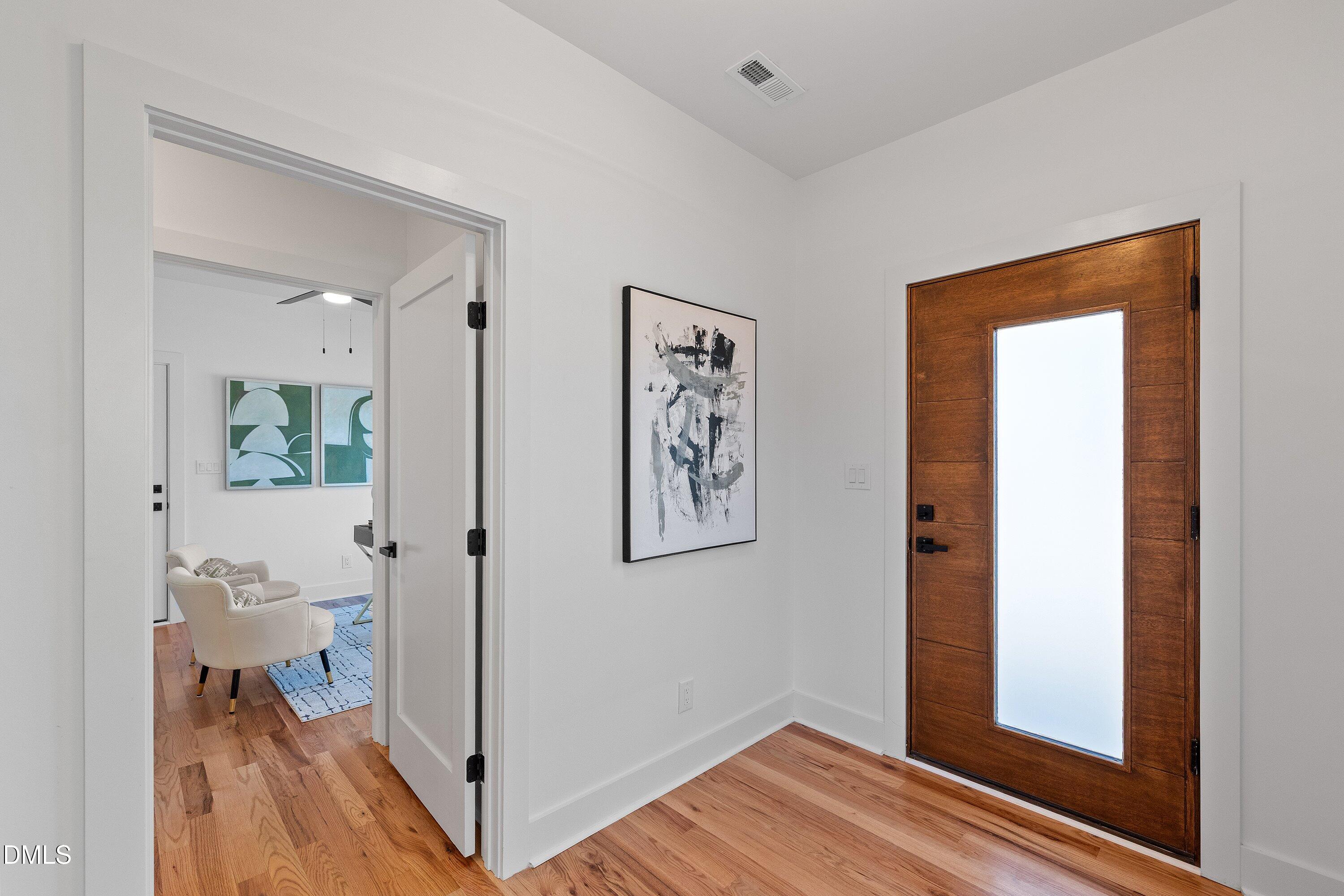 Entryway with a wood-and-glass front door, hardwood floors, and a view into a furnished sitting area.