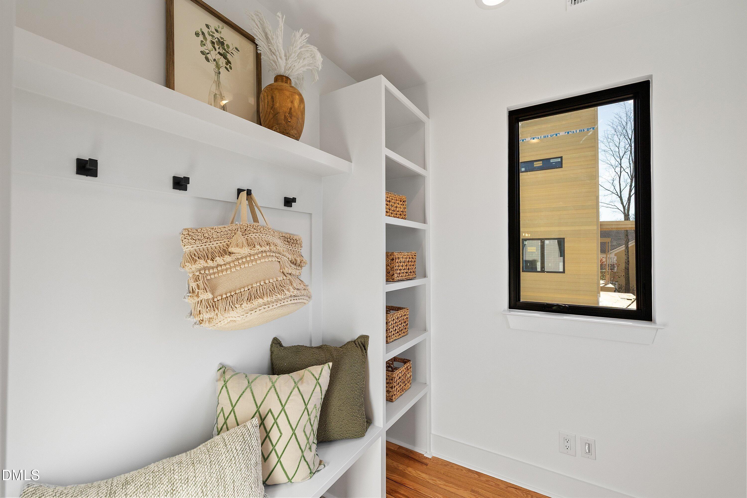 Staged mudroom nook with a built-in bench, black hooks, woven baskets, and a large black-framed window.