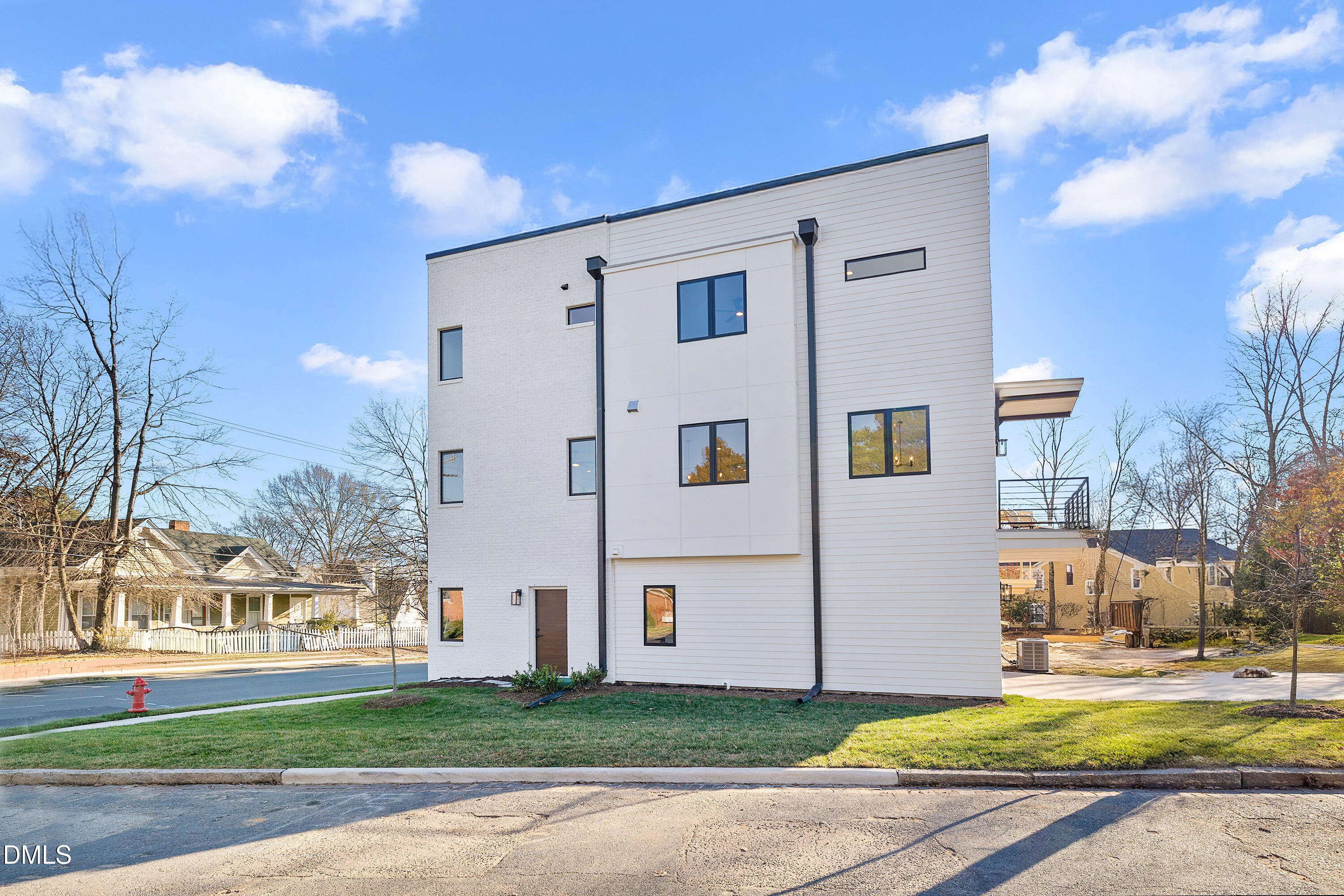 Modern three-story white house with black-framed windows and a side deck on a grassy corner lot.