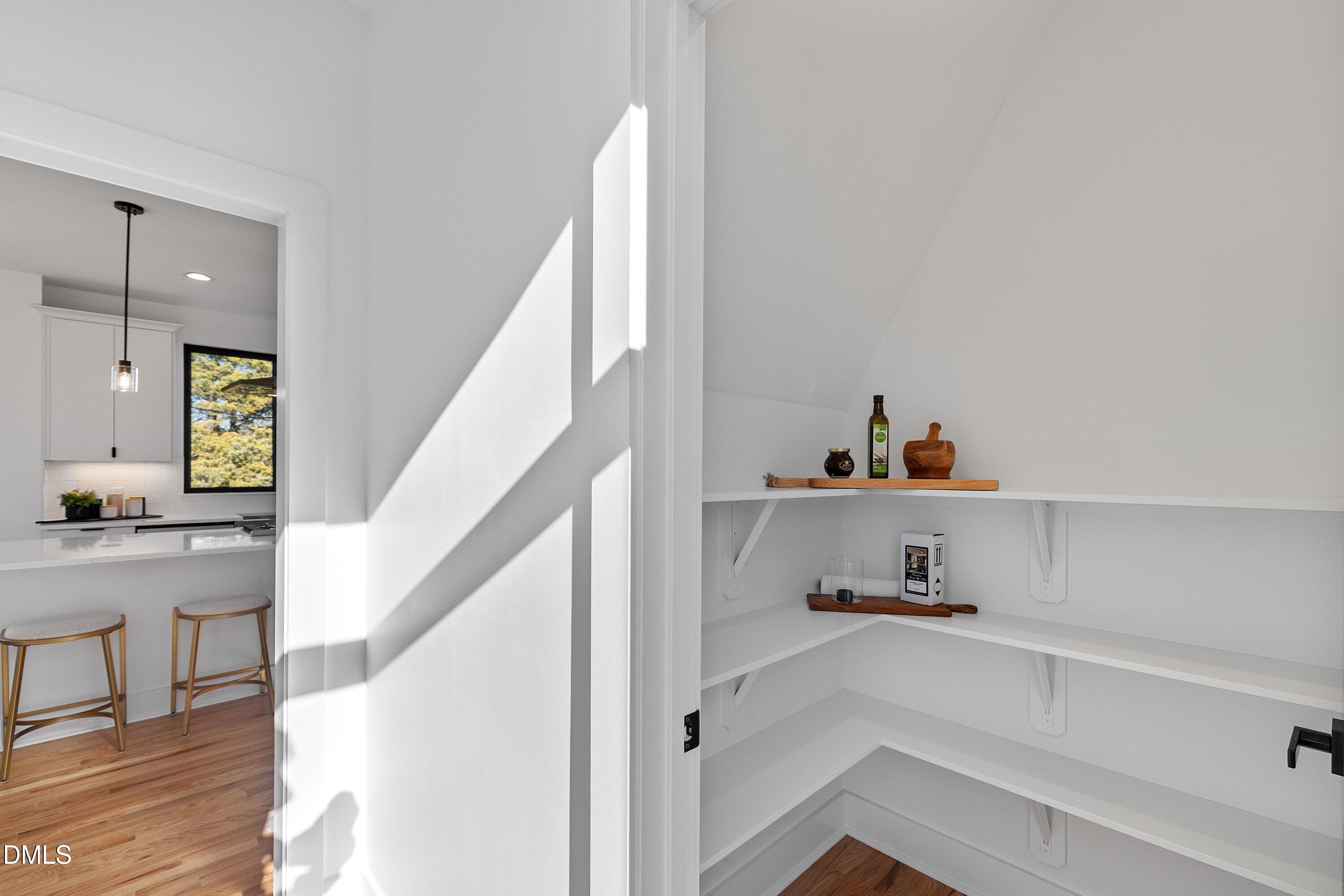 Walk-in pantry with white built-in shelves, viewed beside a kitchen counter with two stools.