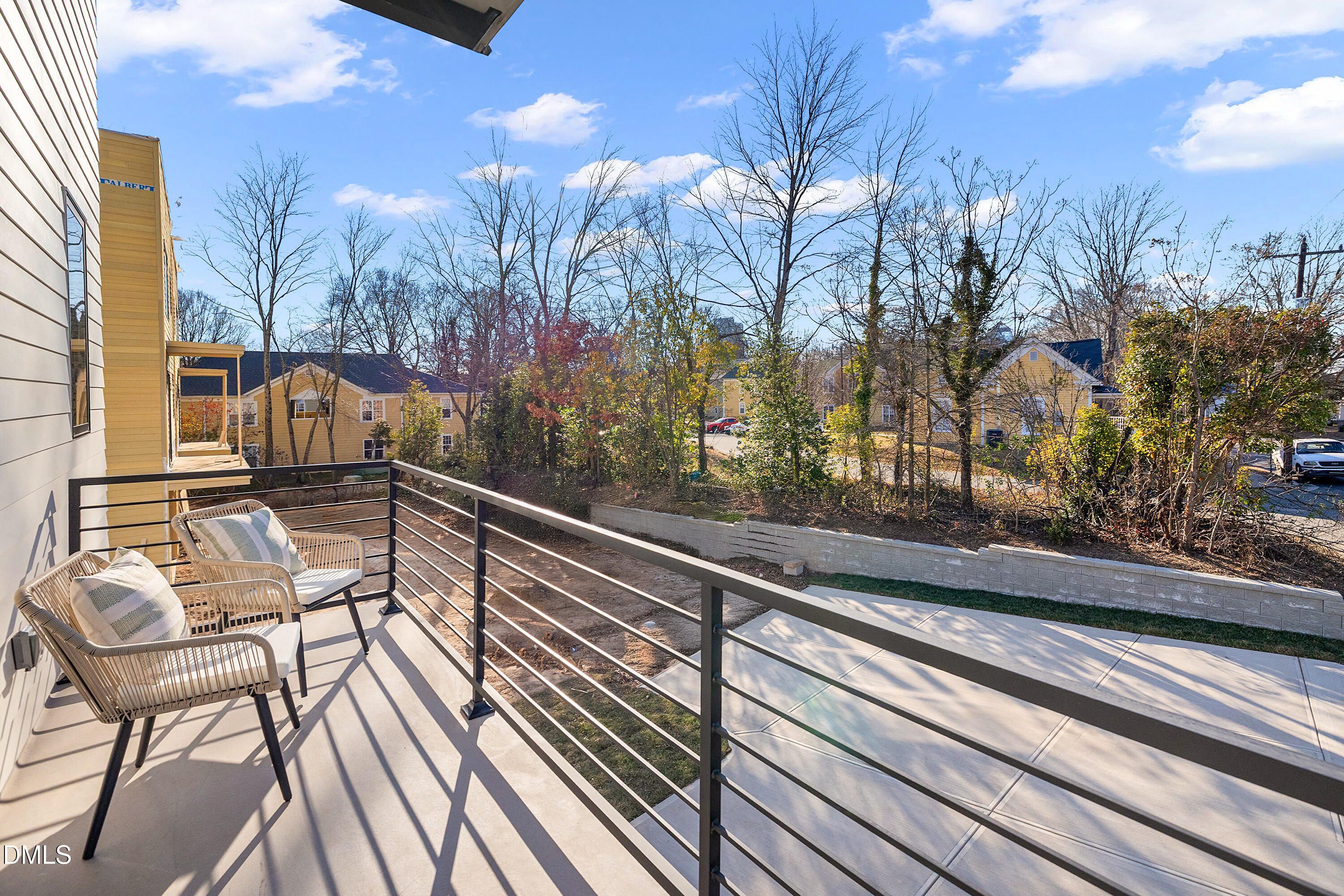 Furnished balcony with woven chairs and black railings overlooking neighboring homes.