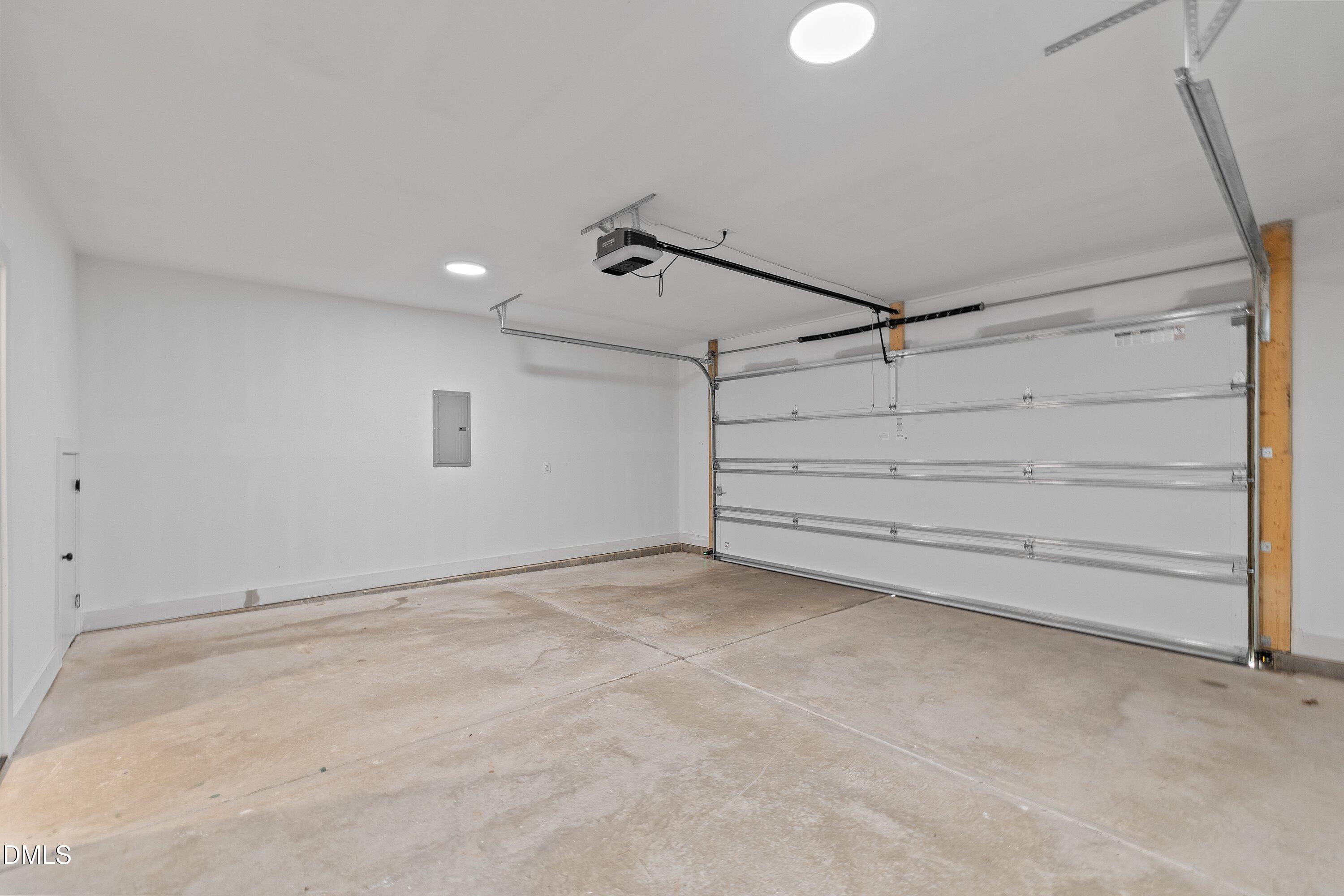 Empty garage with a concrete floor, overhead door, and ceiling-mounted opener.