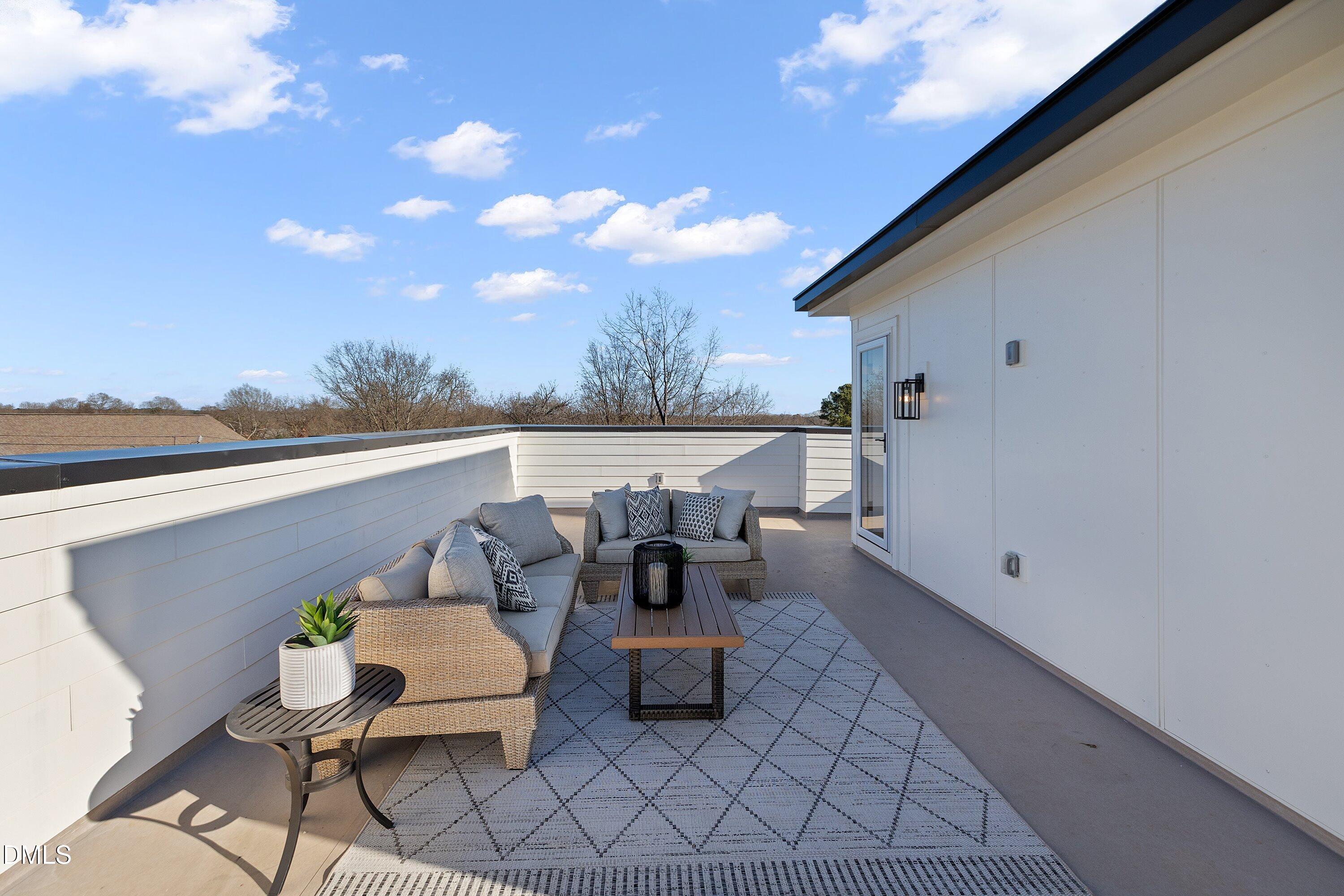 Rooftop terrace with wicker seating, a patterned rug, and white privacy walls.