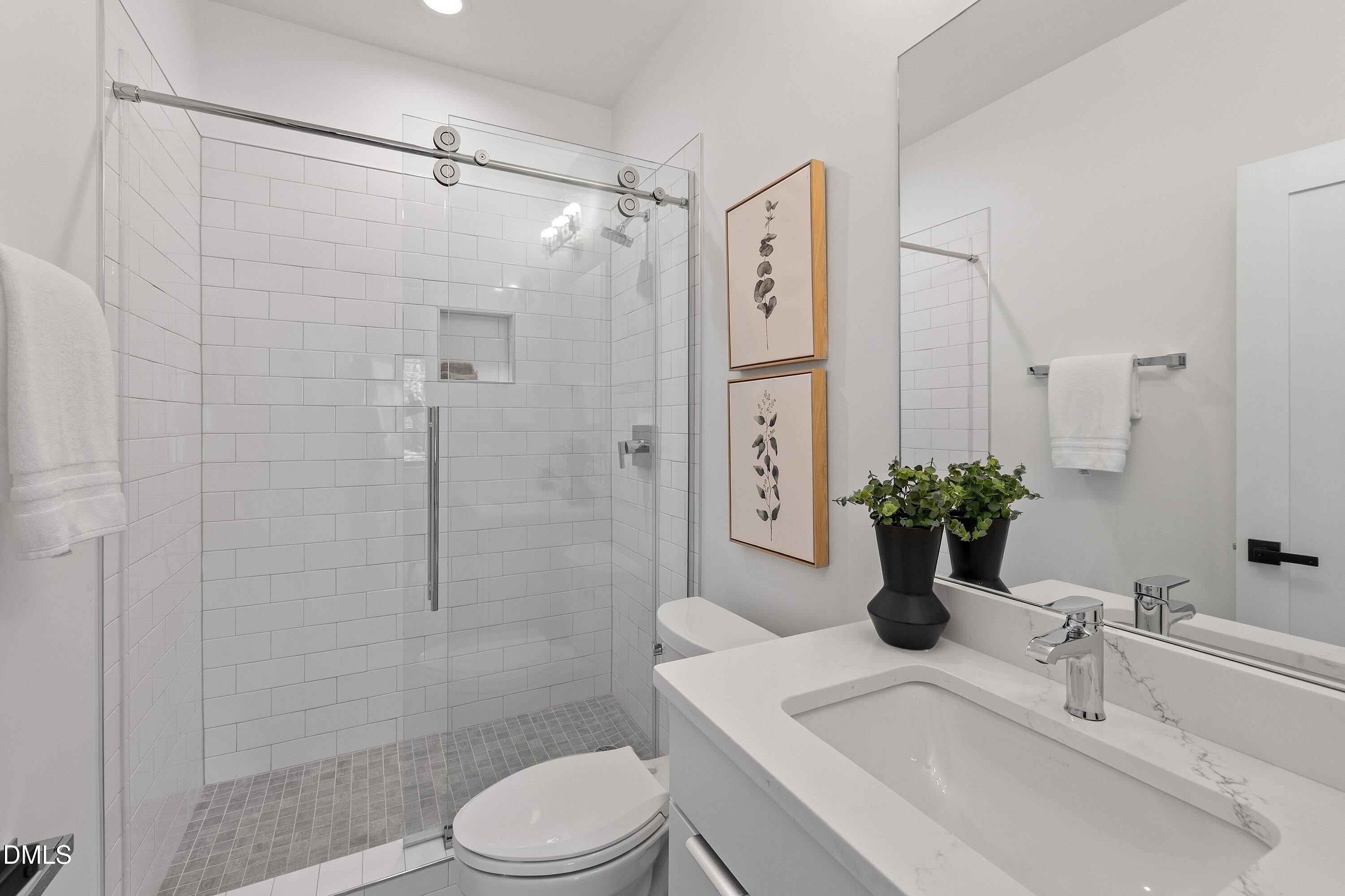 Bathroom with a glass-enclosed subway-tile shower, gray mosaic floor, and white vanity.