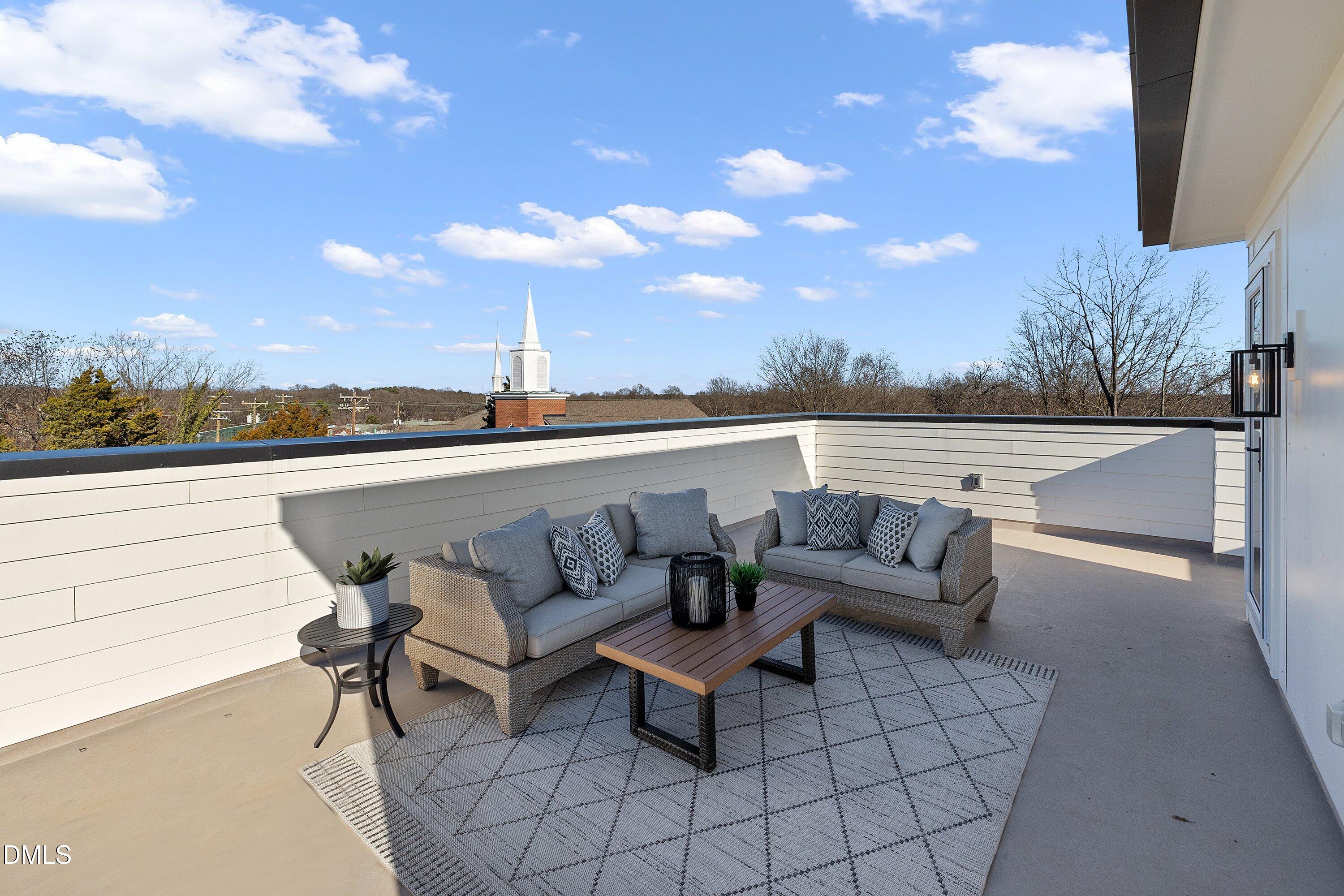 Rooftop terrace with gray sofas and a wood coffee table, overlooking a church steeple.