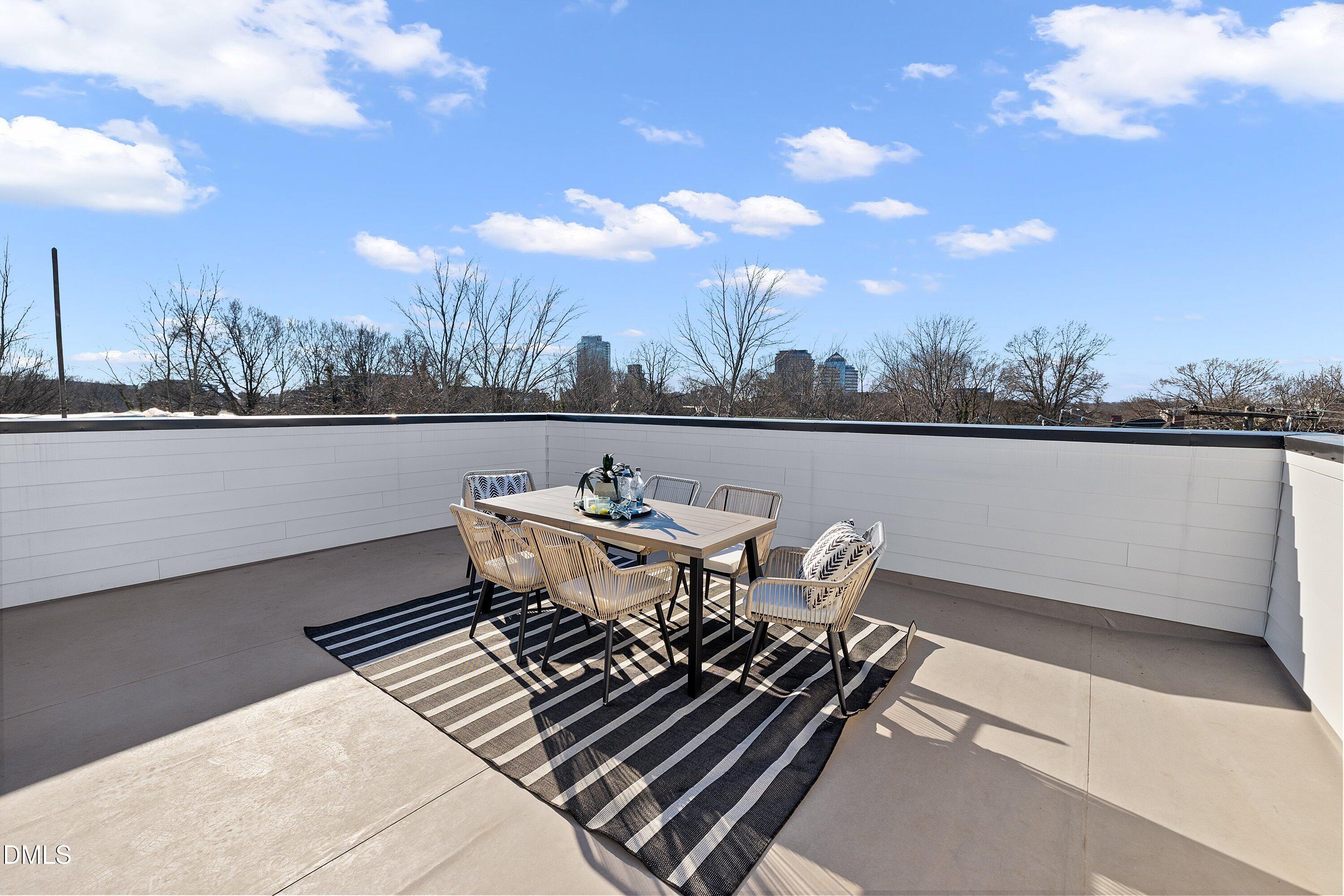 Rooftop terrace with a dining set and striped rug overlooking a distant city skyline.