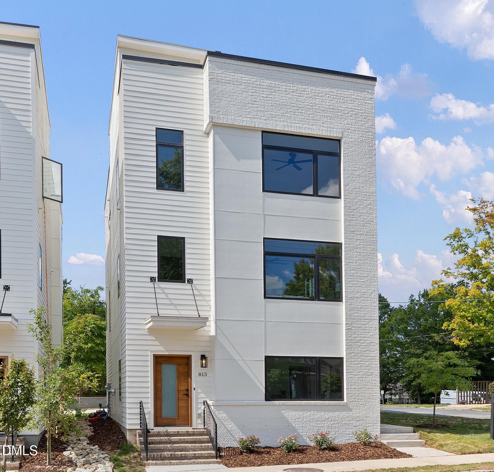 Modern three-story white house with brick facade, dark windows, and a wood front door.