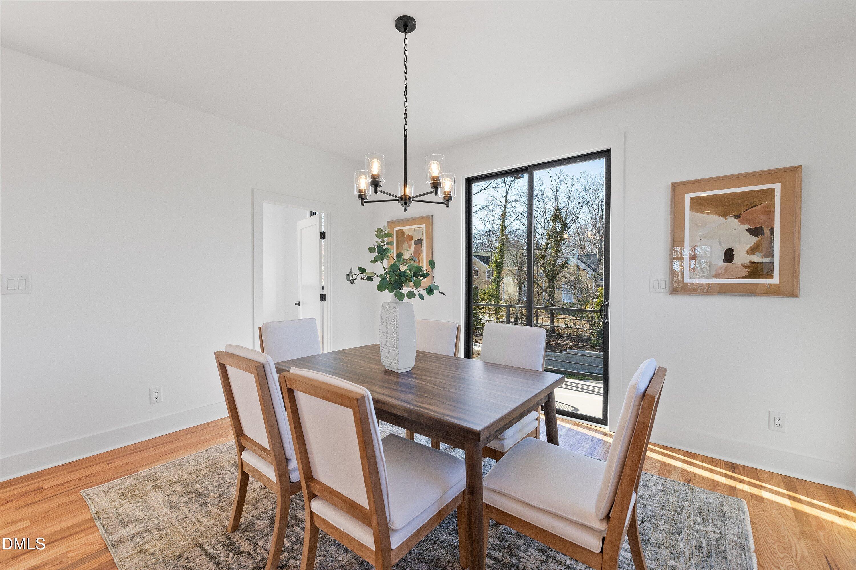 Staged dining room with a wood table, modern chandelier, and sliding glass door to a balcony.