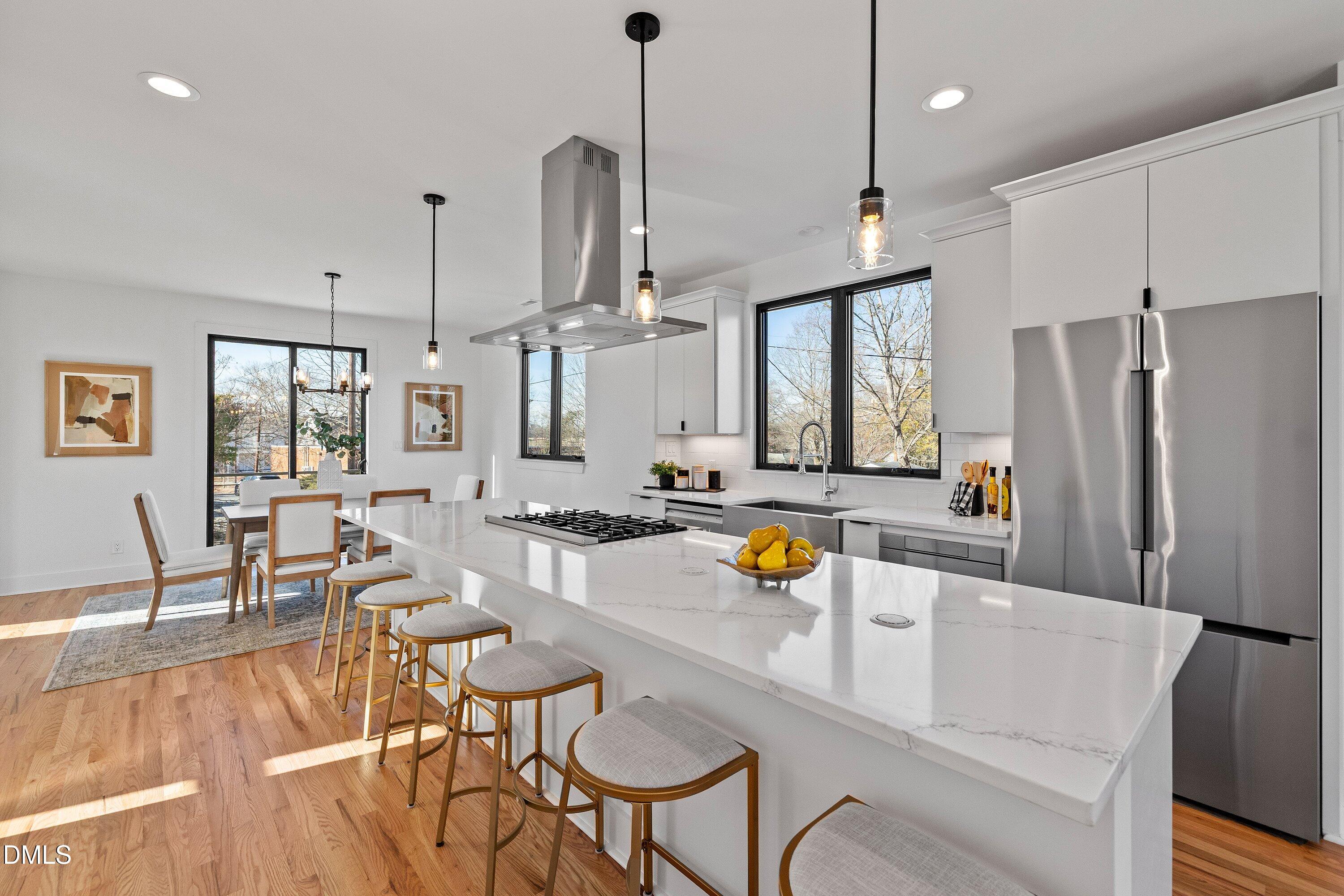 Open-plan kitchen with a long quartz island, gas cooktop, stainless appliances, and adjoining dining area.