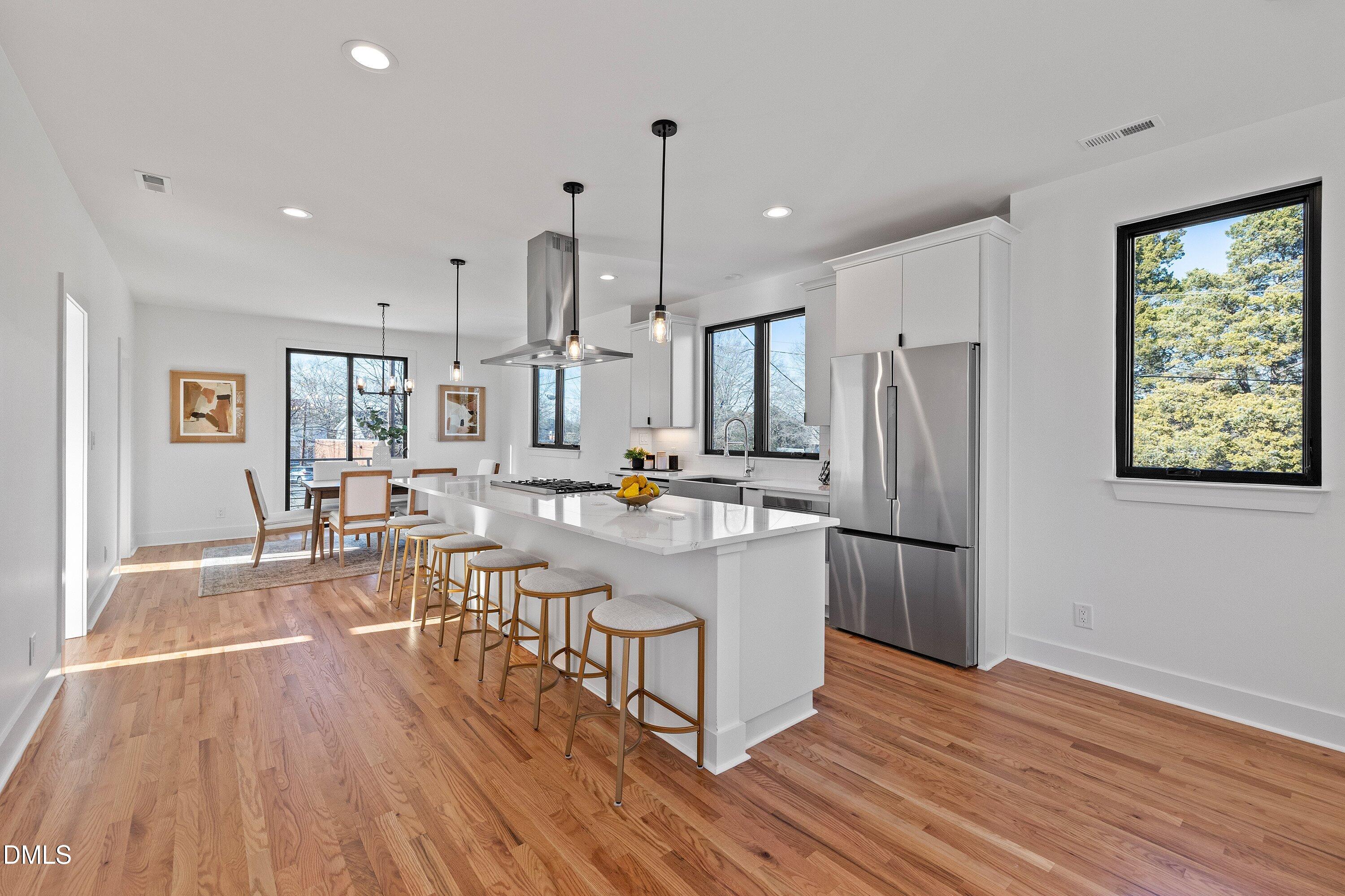 Open kitchen and dining area with a white island, stainless steel appliances, and warm hardwood floors.