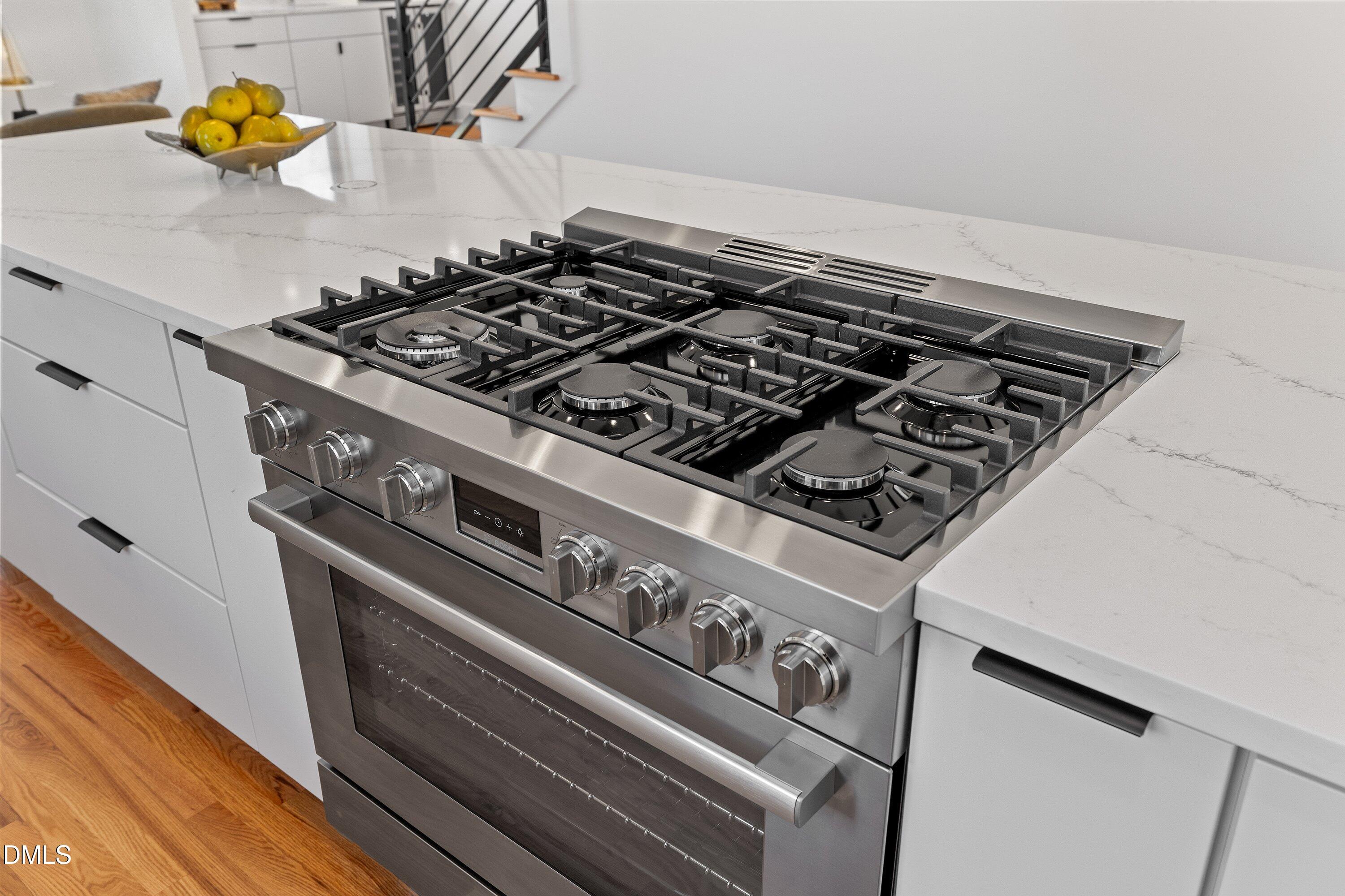 Stainless-steel gas range with multiple burners set into a white quartz kitchen island.