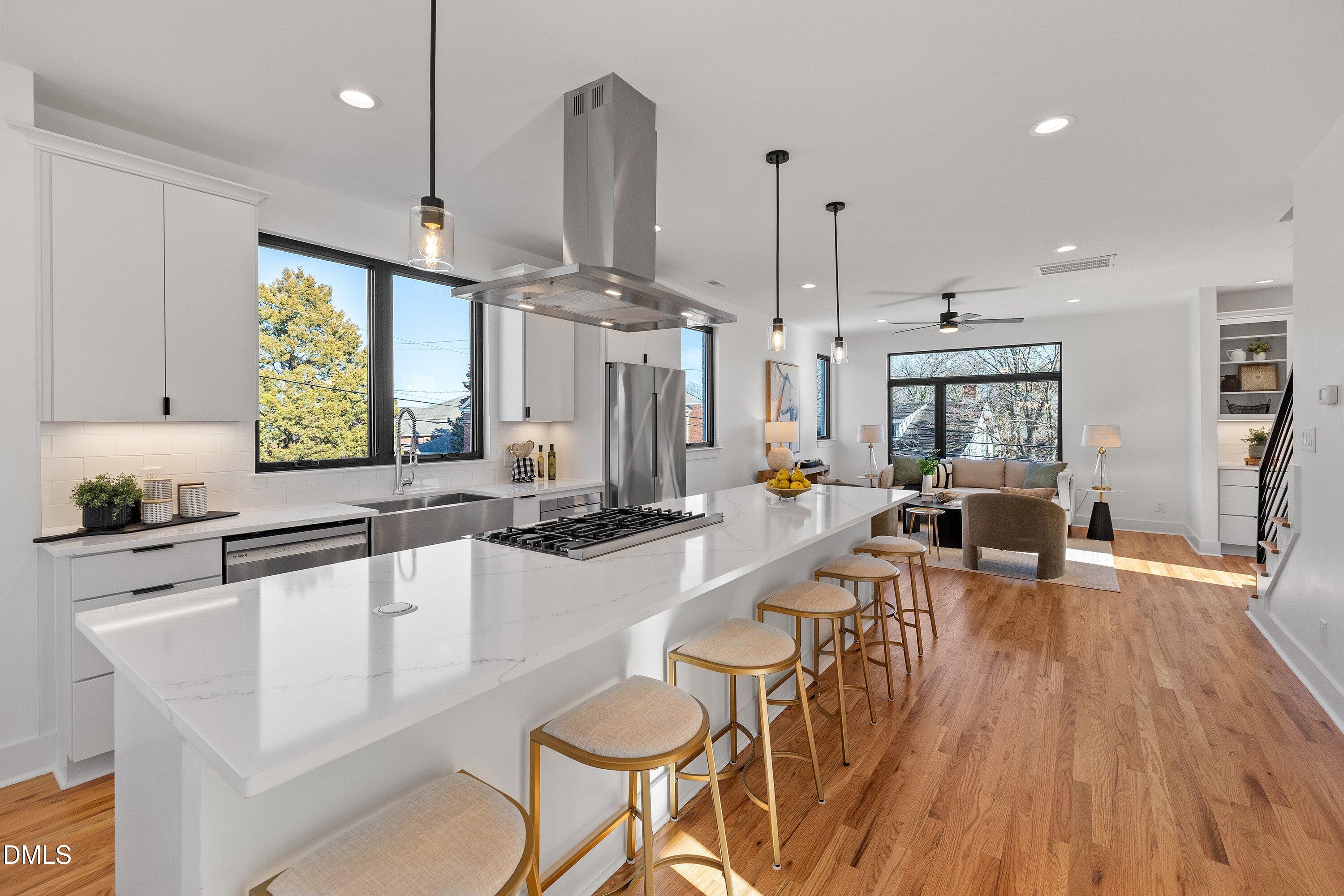 Open-plan kitchen and living area with a long quartz island, breakfast stools, and hardwood floors.