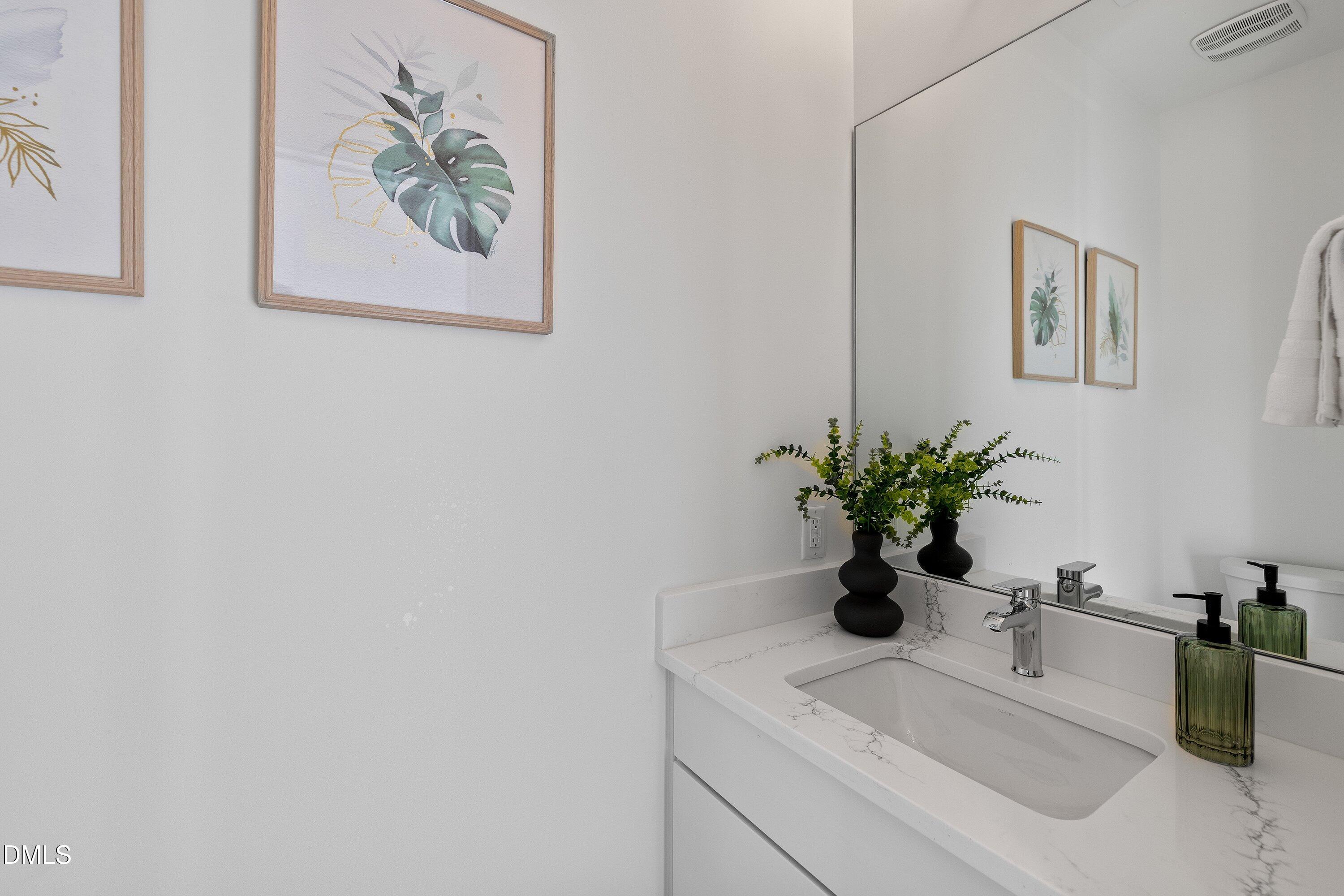 Bathroom vanity with a large mirror, marble-look counter, chrome faucet, and botanical accents.