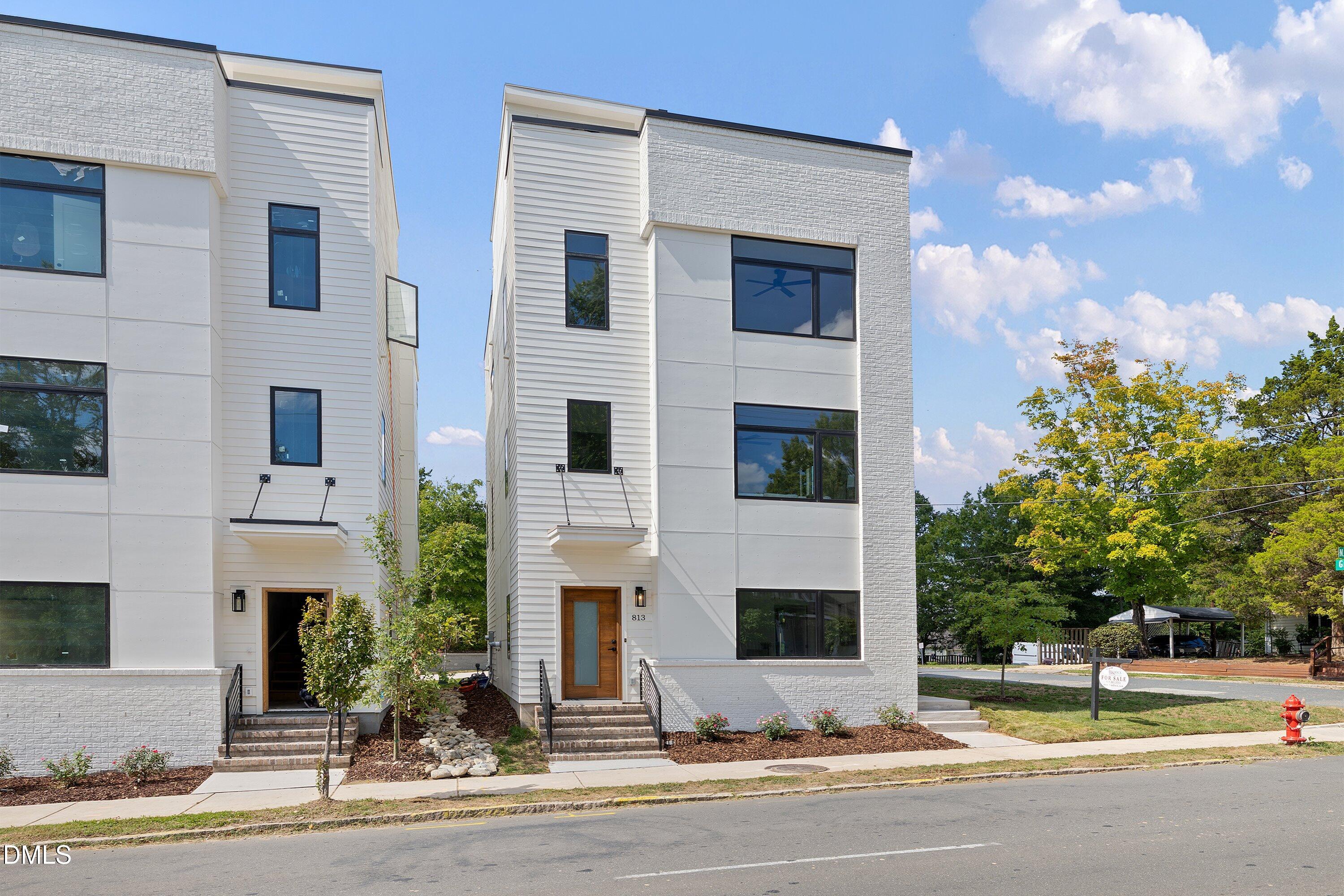 Modern white townhouse with dark-framed windows and a wood entry door at the sidewalk.