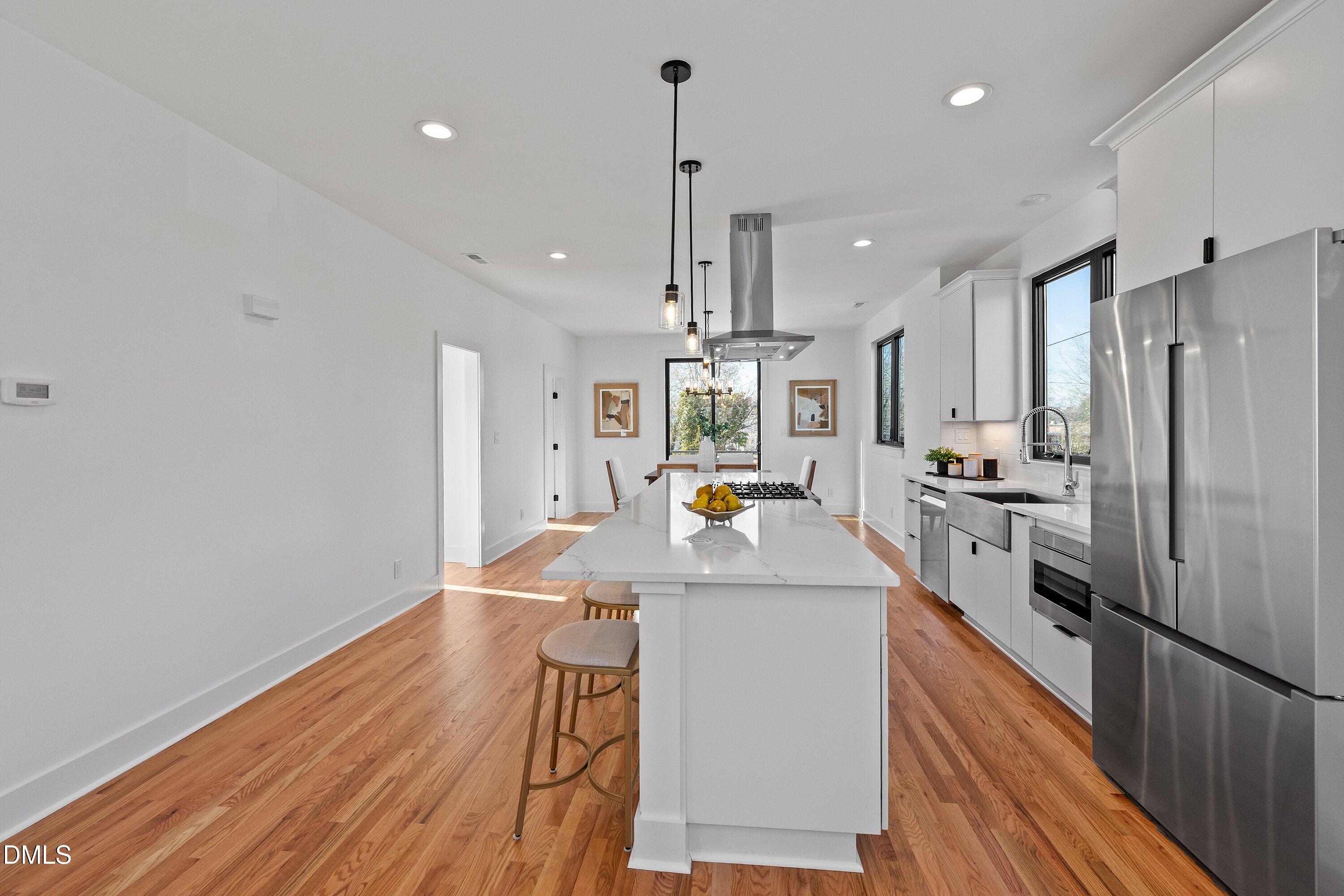 Modern kitchen with a large quartz island, stainless steel appliances, and warm wood floors.