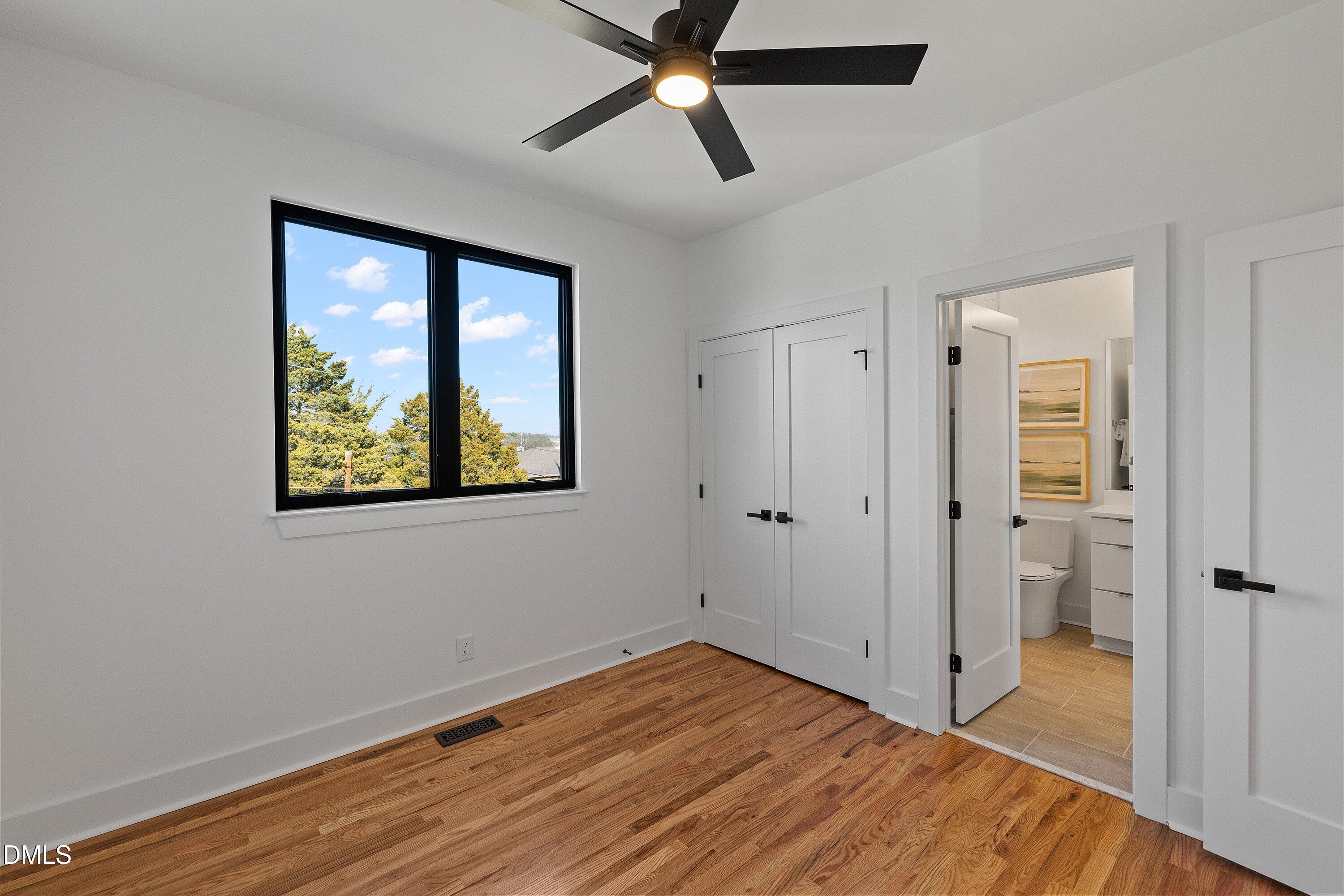 Unfurnished bedroom with hardwood floors, a large window, and an adjoining bathroom.
