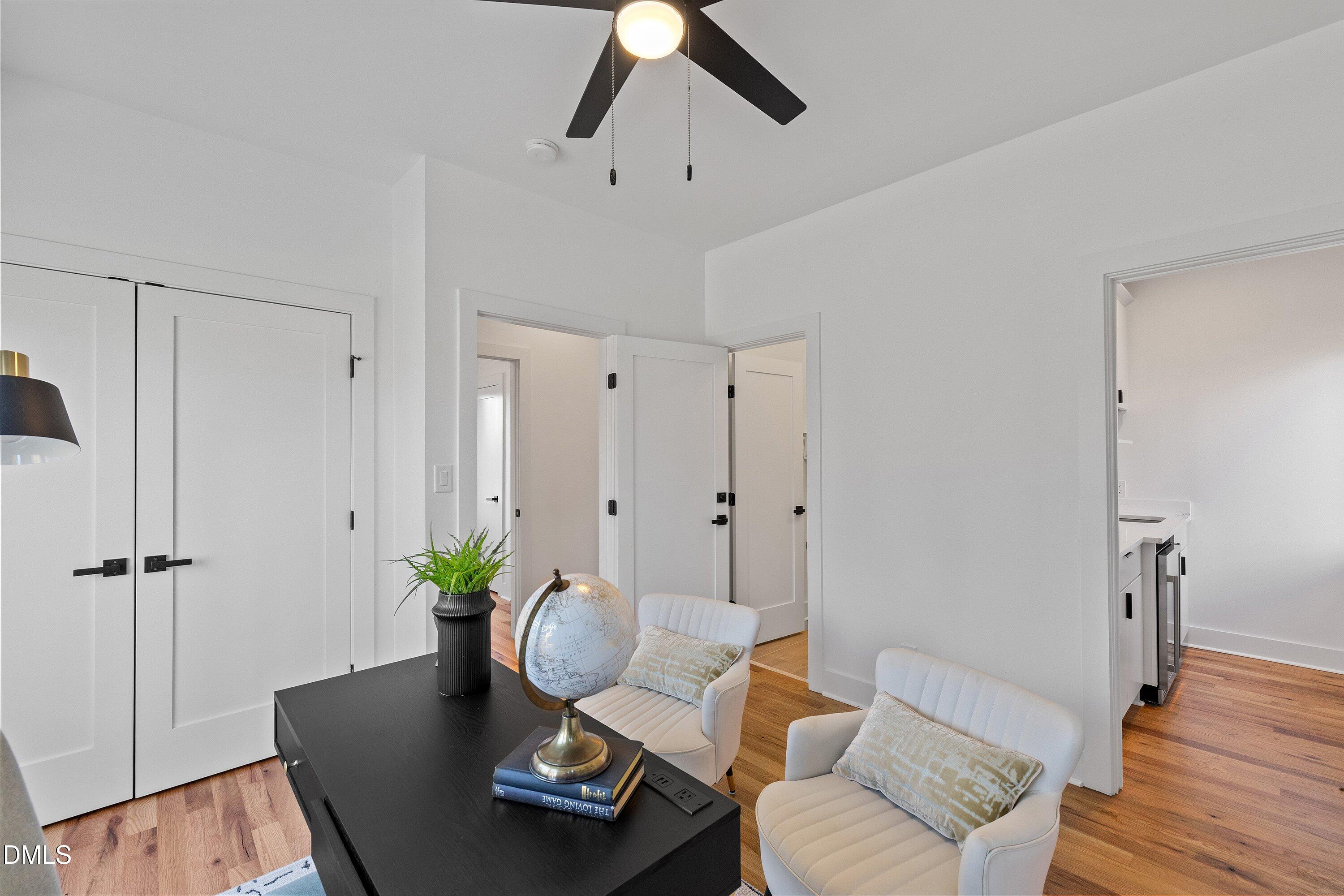 Staged home office with a black desk, white chairs, a globe, and warm hardwood floors.