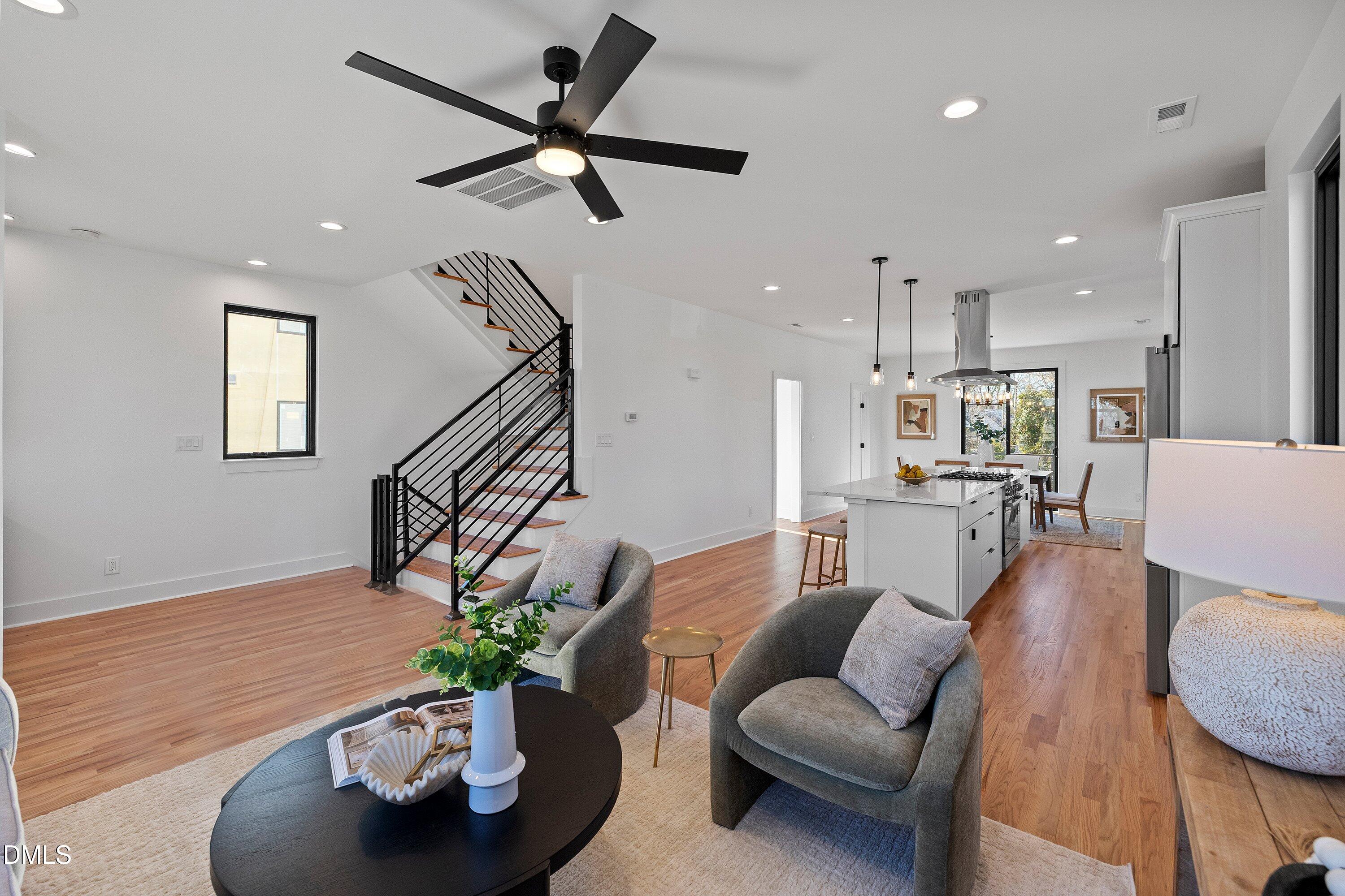 Open-plan living room and kitchen with wood floors, gray armchairs, and a black metal staircase.