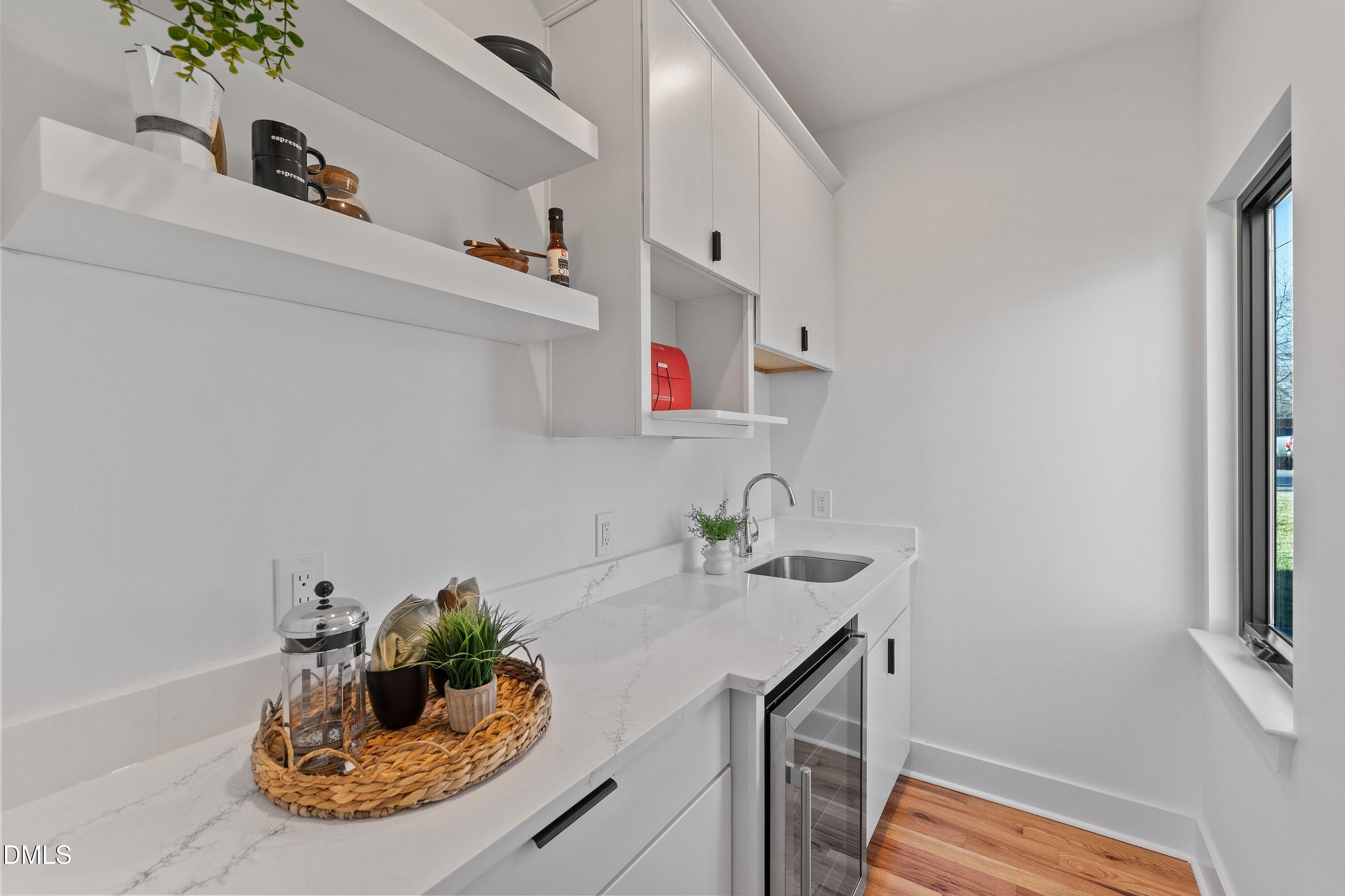 Modern white kitchen with floating shelves, veined counters, a stainless sink, and hardwood floors.