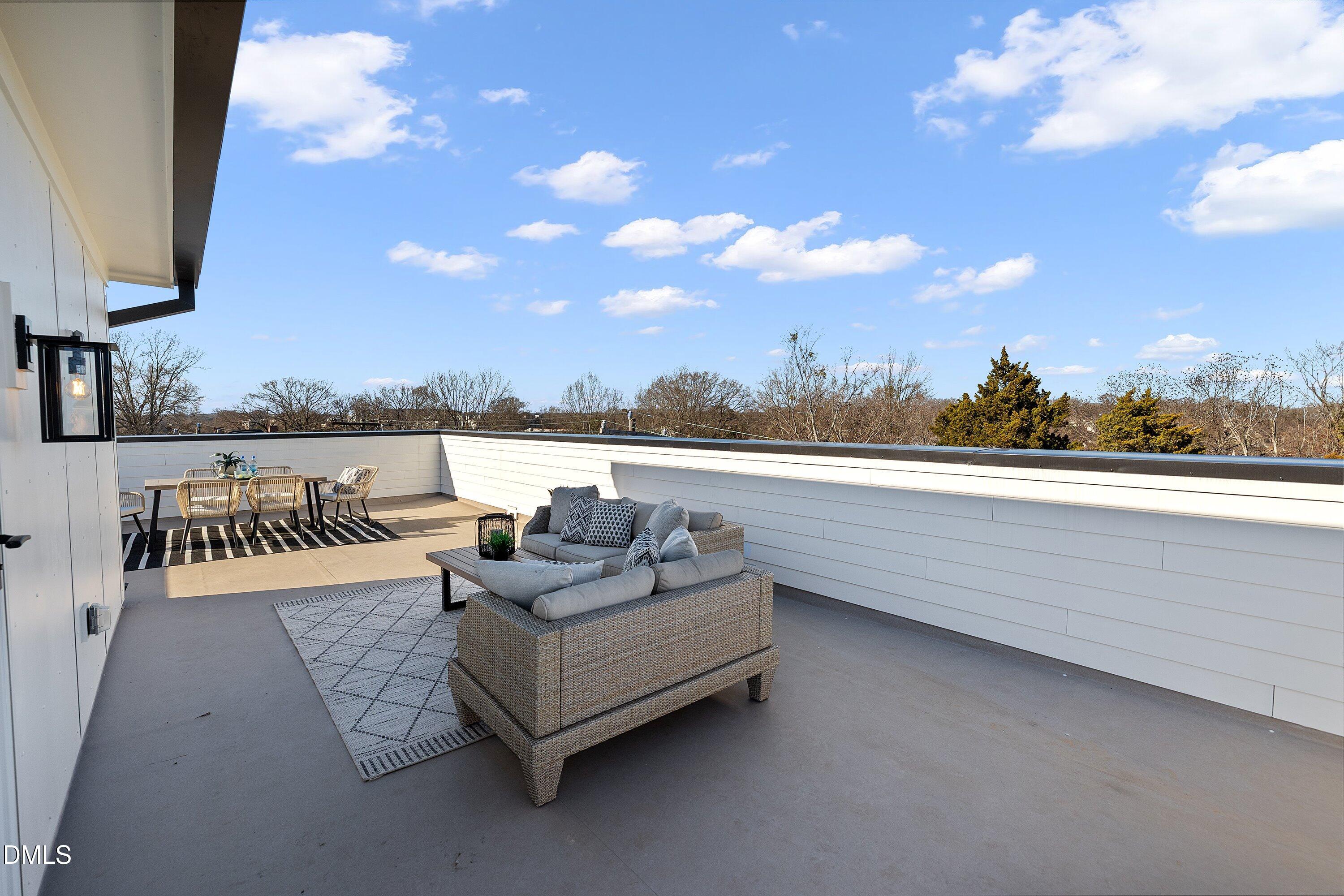 Rooftop terrace with wicker lounge seating and dining area overlooking trees.