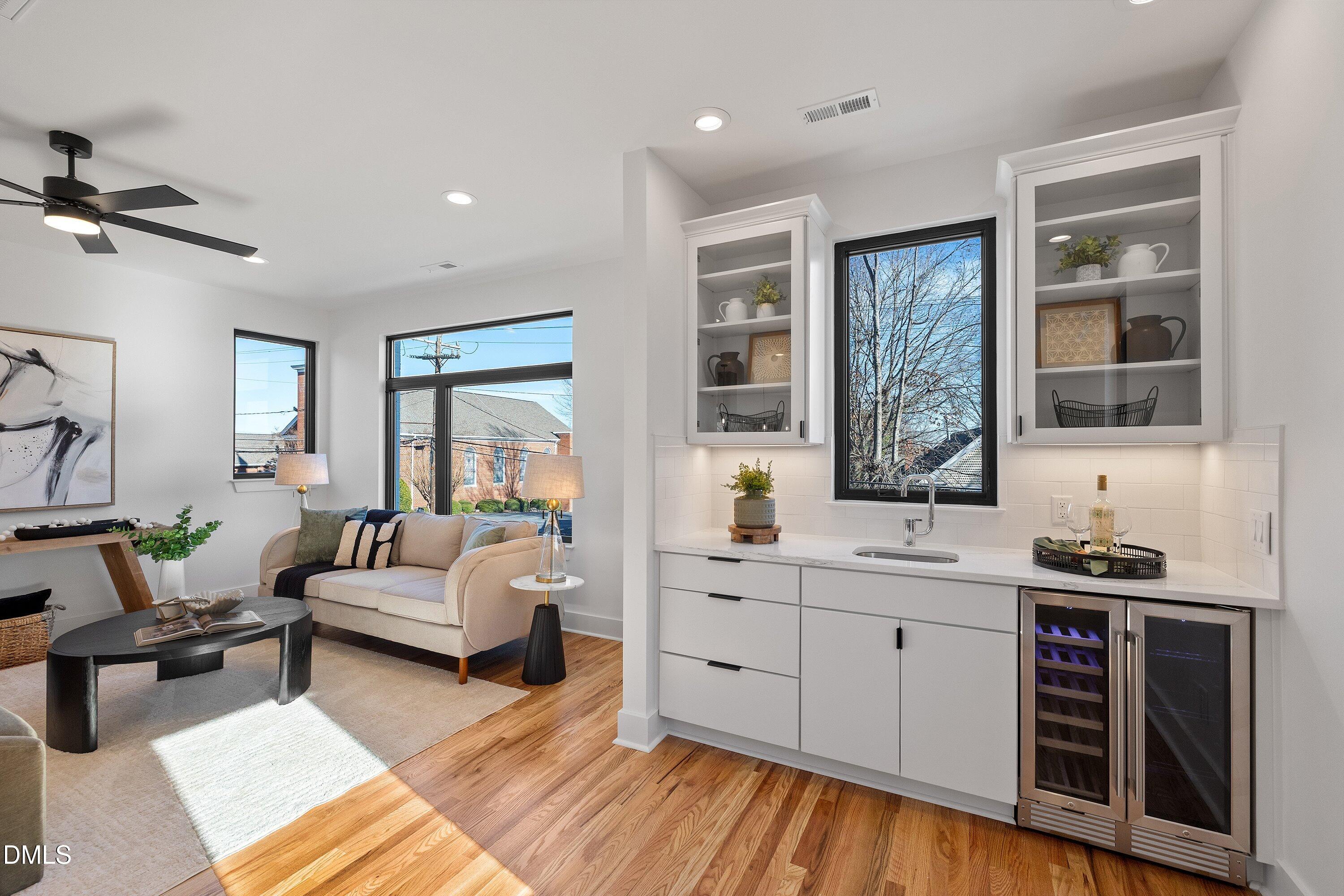 Open-plan living room and built-in bar with large windows, glass-front cabinets, and dual wine refrigerators.