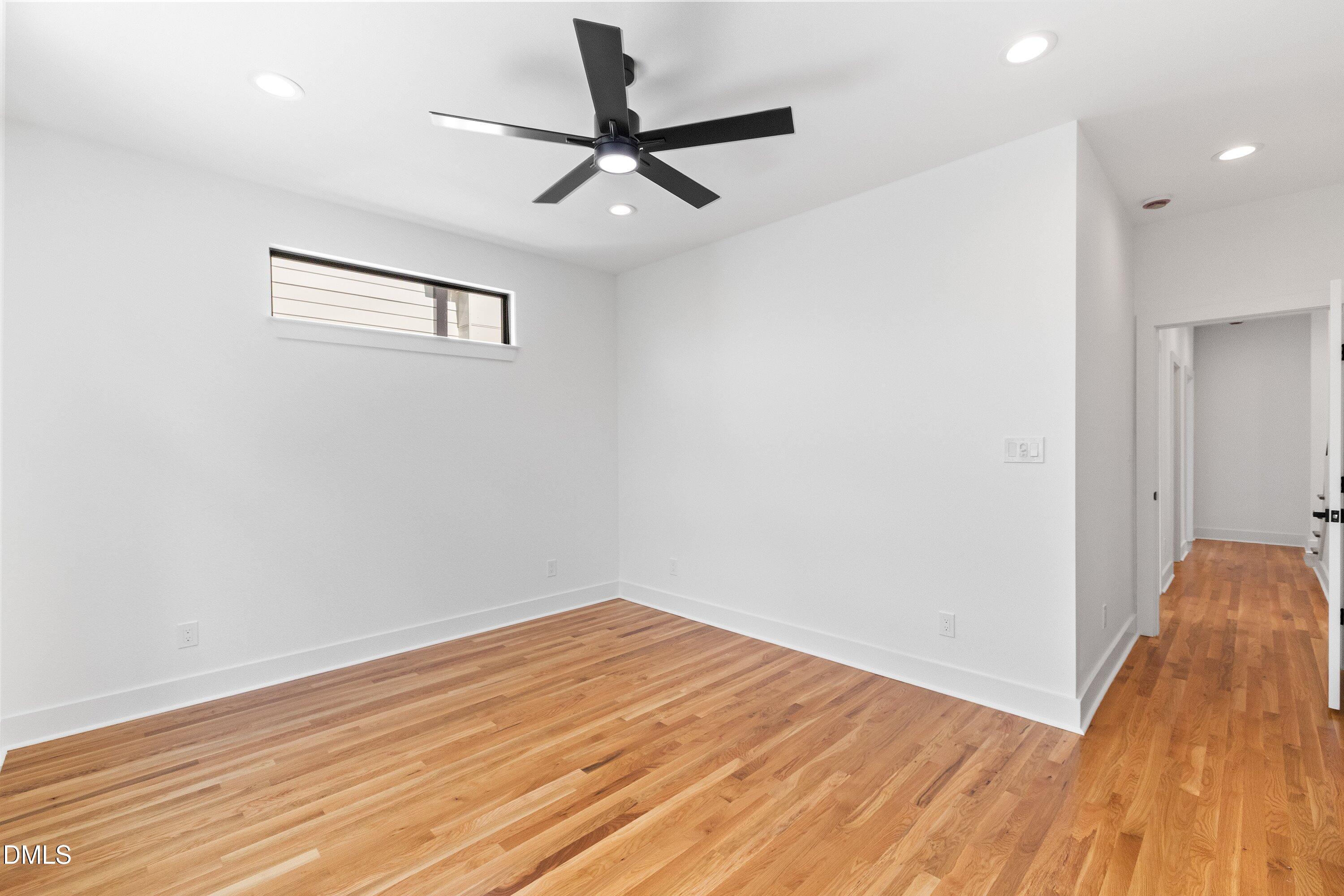 Vacant room with hardwood floors, a black ceiling fan, and a doorway to the hall.