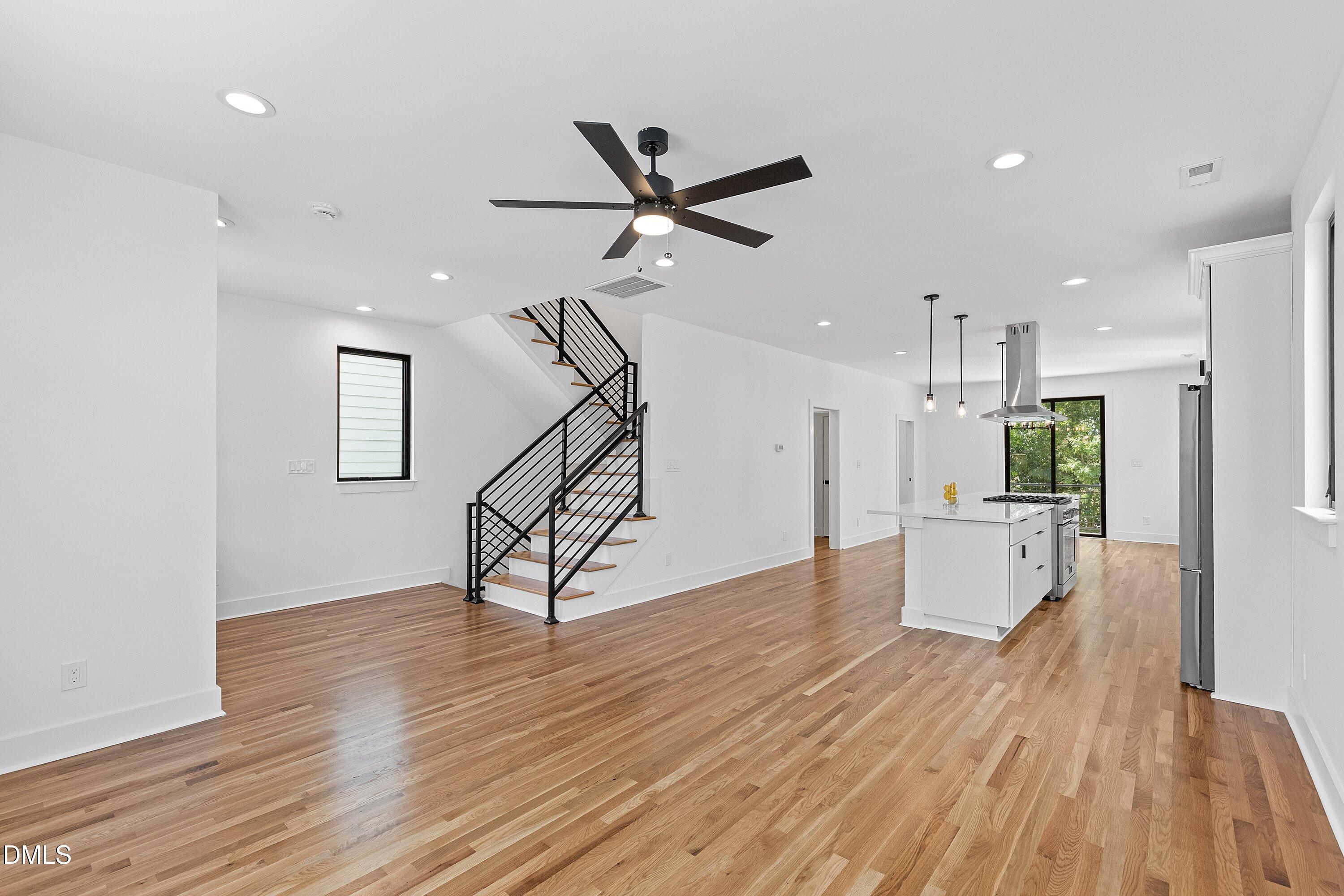 Open-plan kitchen and living area with wood floors, a white island, and a black metal staircase.