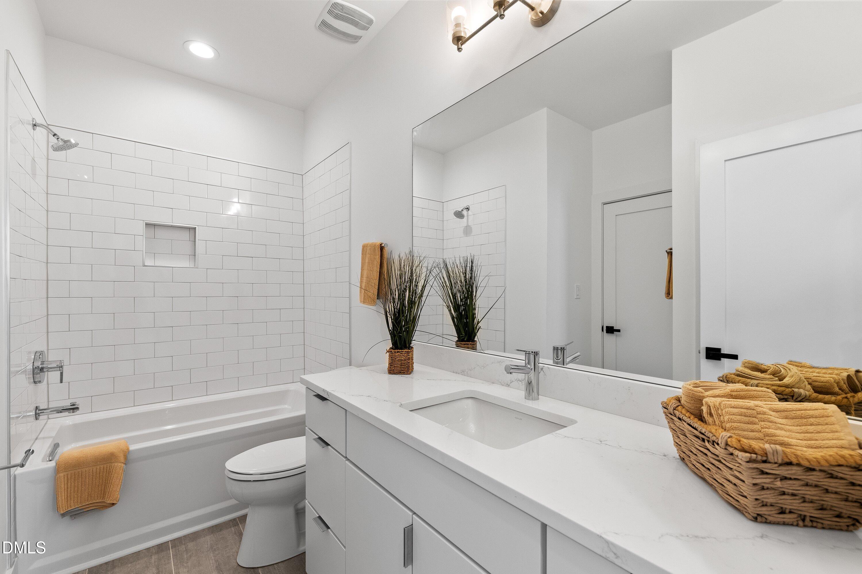 Bathroom with a white subway-tile tub and shower, mirrored wall, and marble-look vanity with mustard towels.
