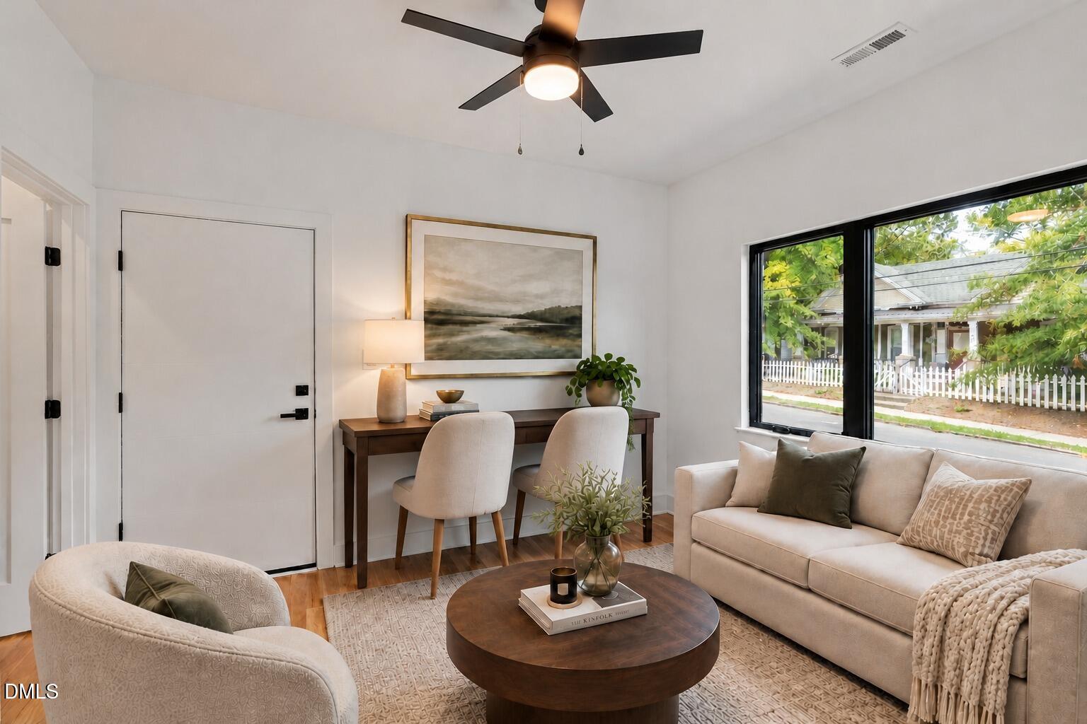 Staged living room with cream seating, a round wood coffee table, and a large street-facing window.